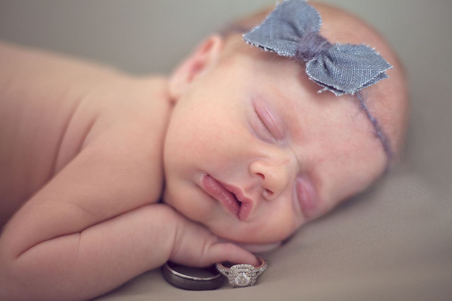 Sleeping newborn wearing a blue bow headband rests next to a ring.