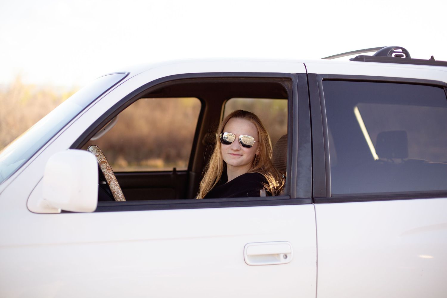 Person driving white SUV with sunglasses during golden hour lighting.