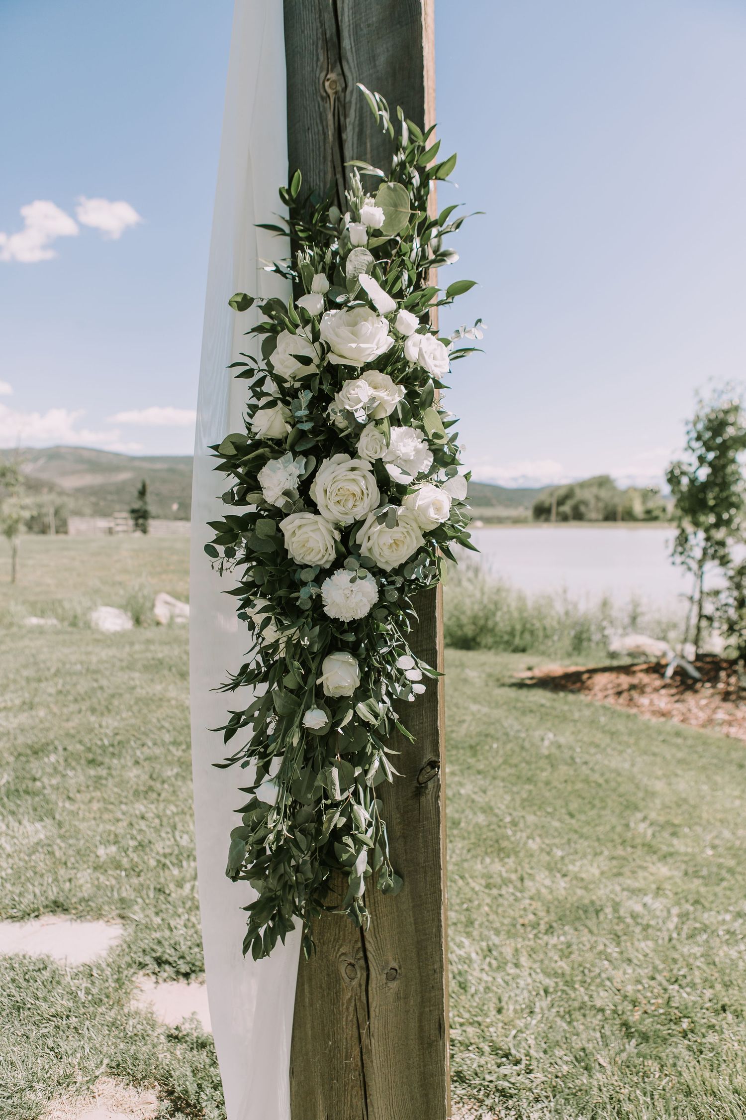 White rose and greenery floral arrangement adorning a wooden post outdoors.