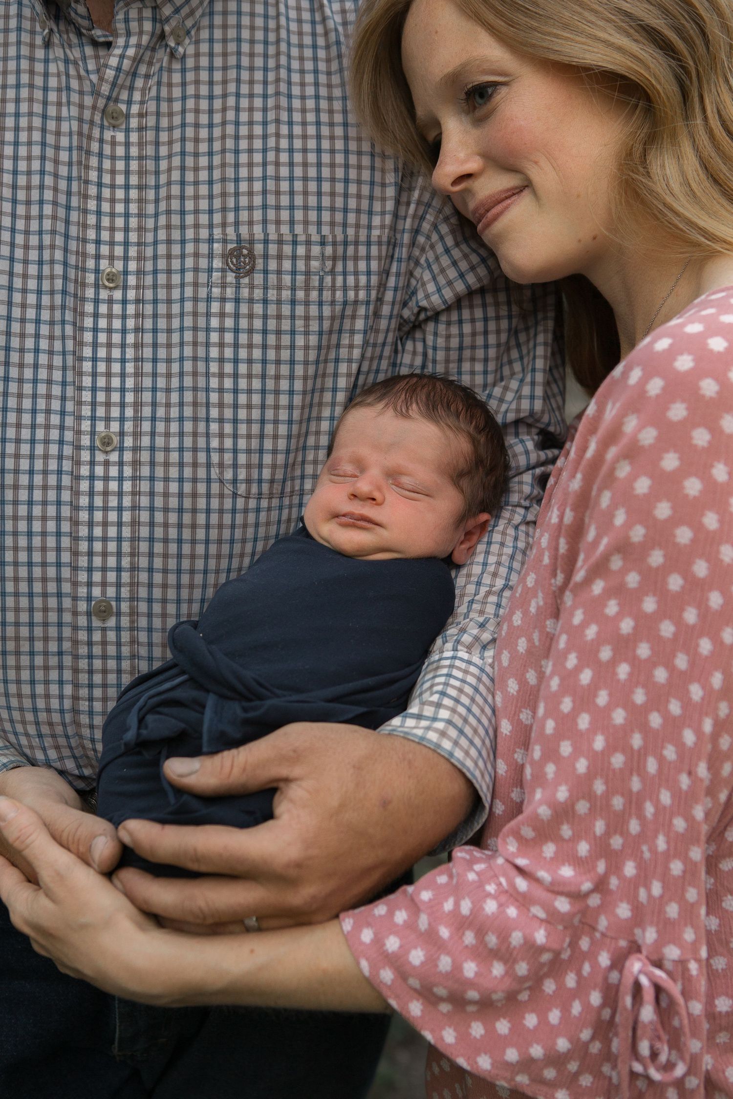 An intimate family moment with a sleeping newborn baby wrapped in navy blue.