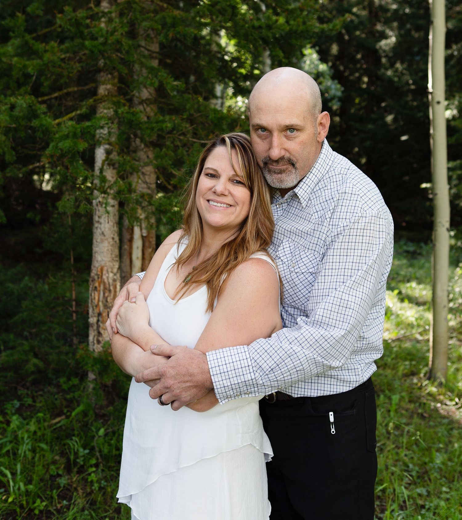 A couple embraces outdoors in a casual portrait against a green forest background.