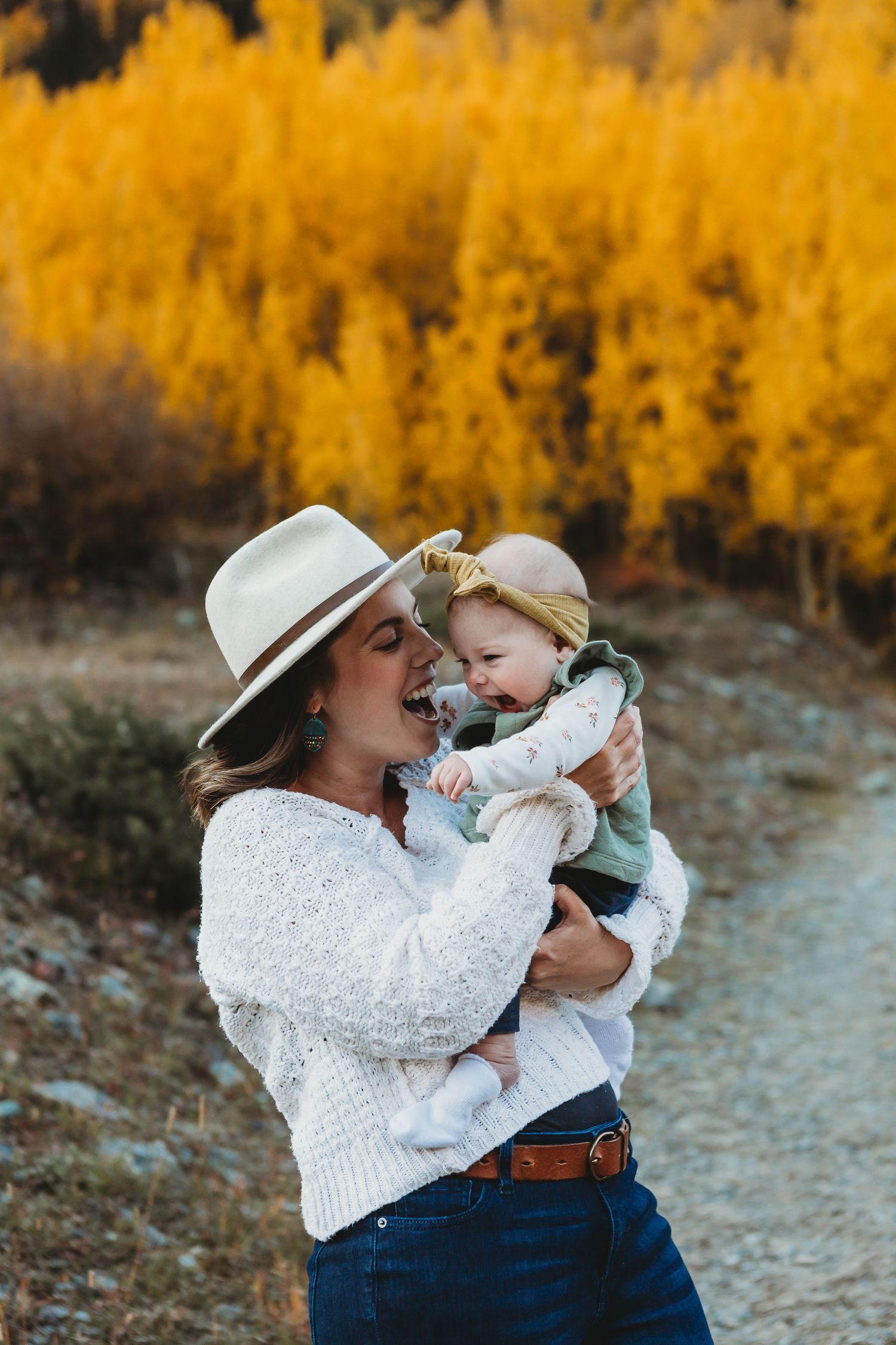 Cozy autumn scene with sweater-clad parent holding baby against backdrop of vibrant golden aspen trees on mountain trail.