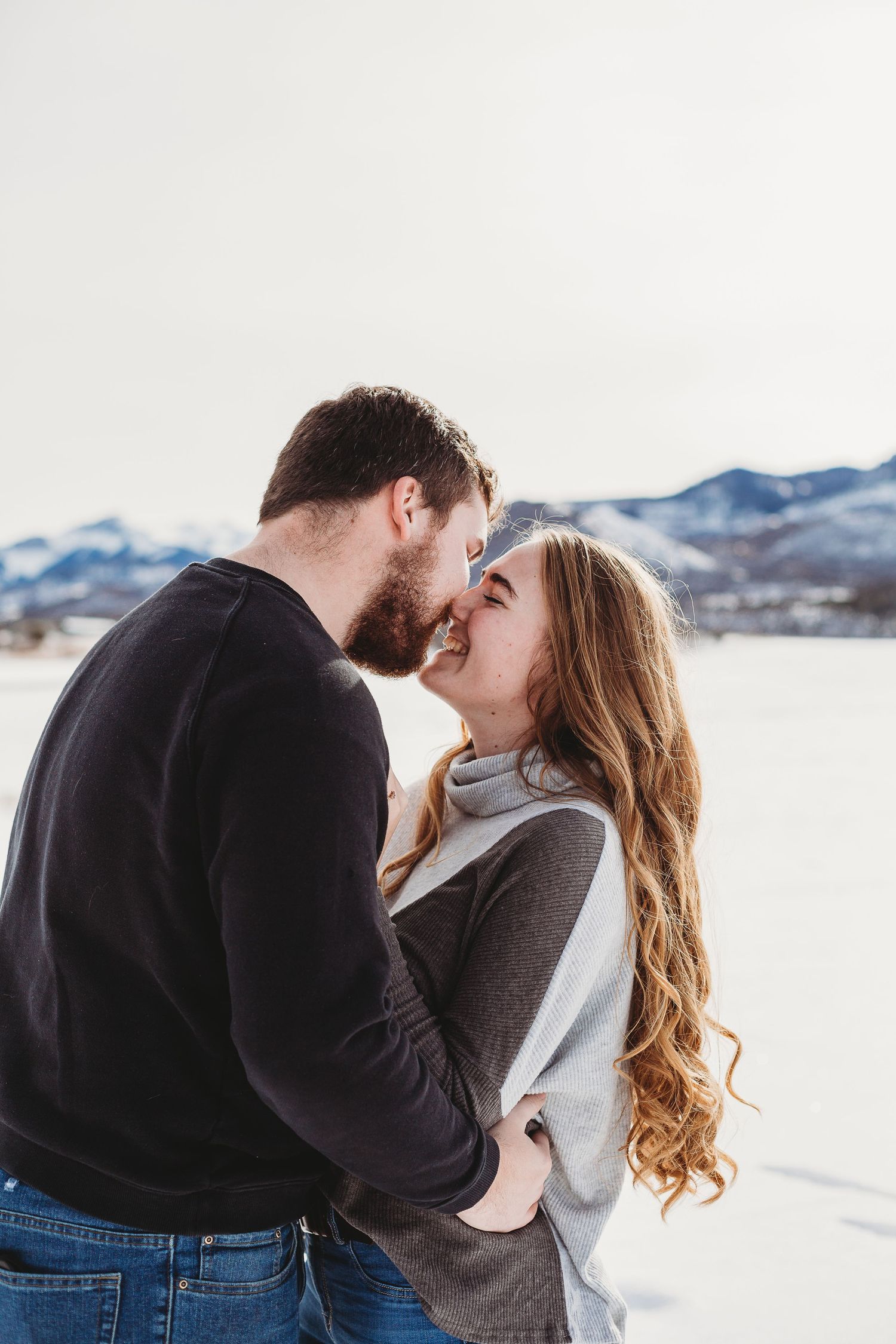 An intimate portrait of a couple sharing a romantic moment in a winter mountain setting.