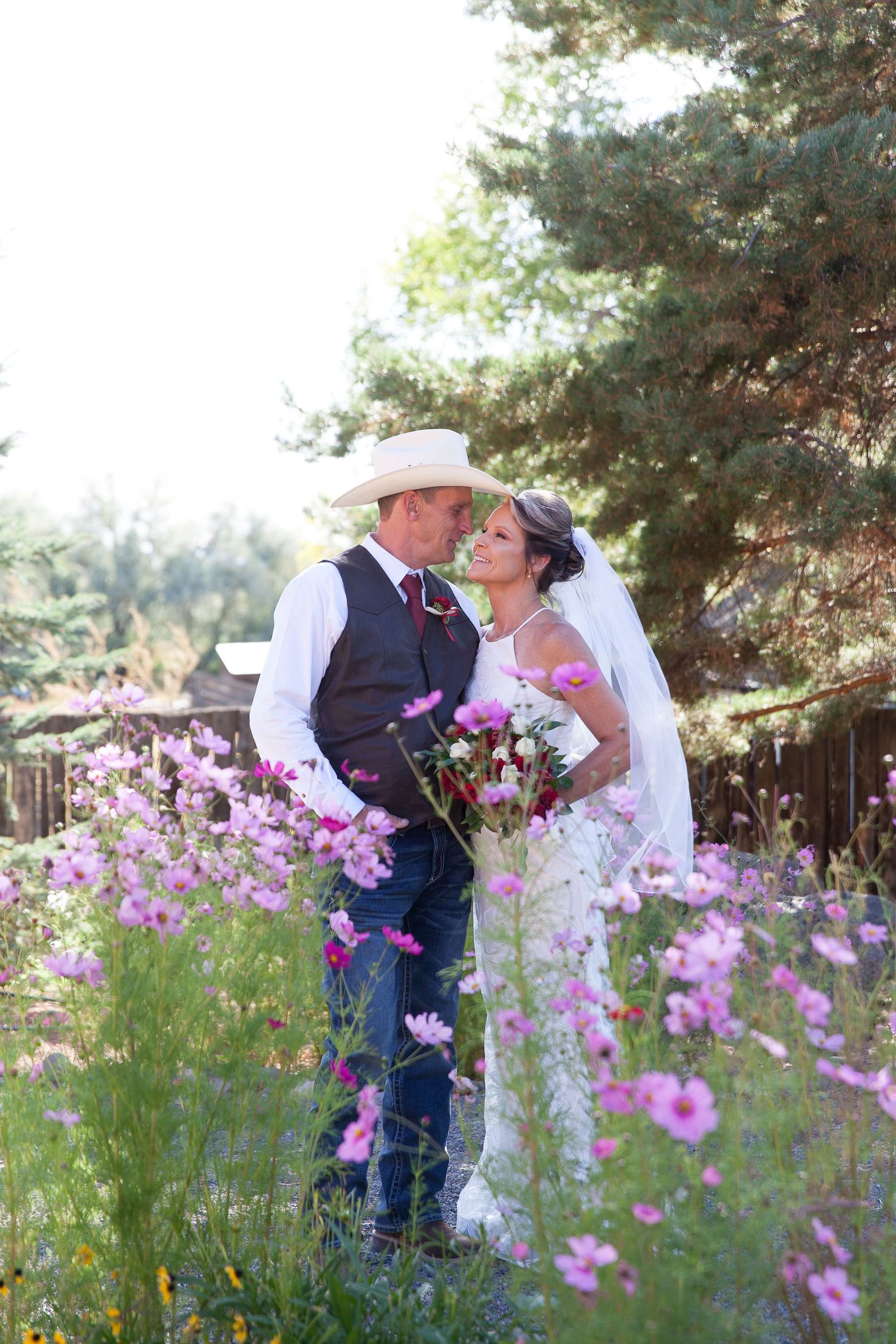 A romantic wedding couple embraces in a field of pink cosmos flowers on their special day.