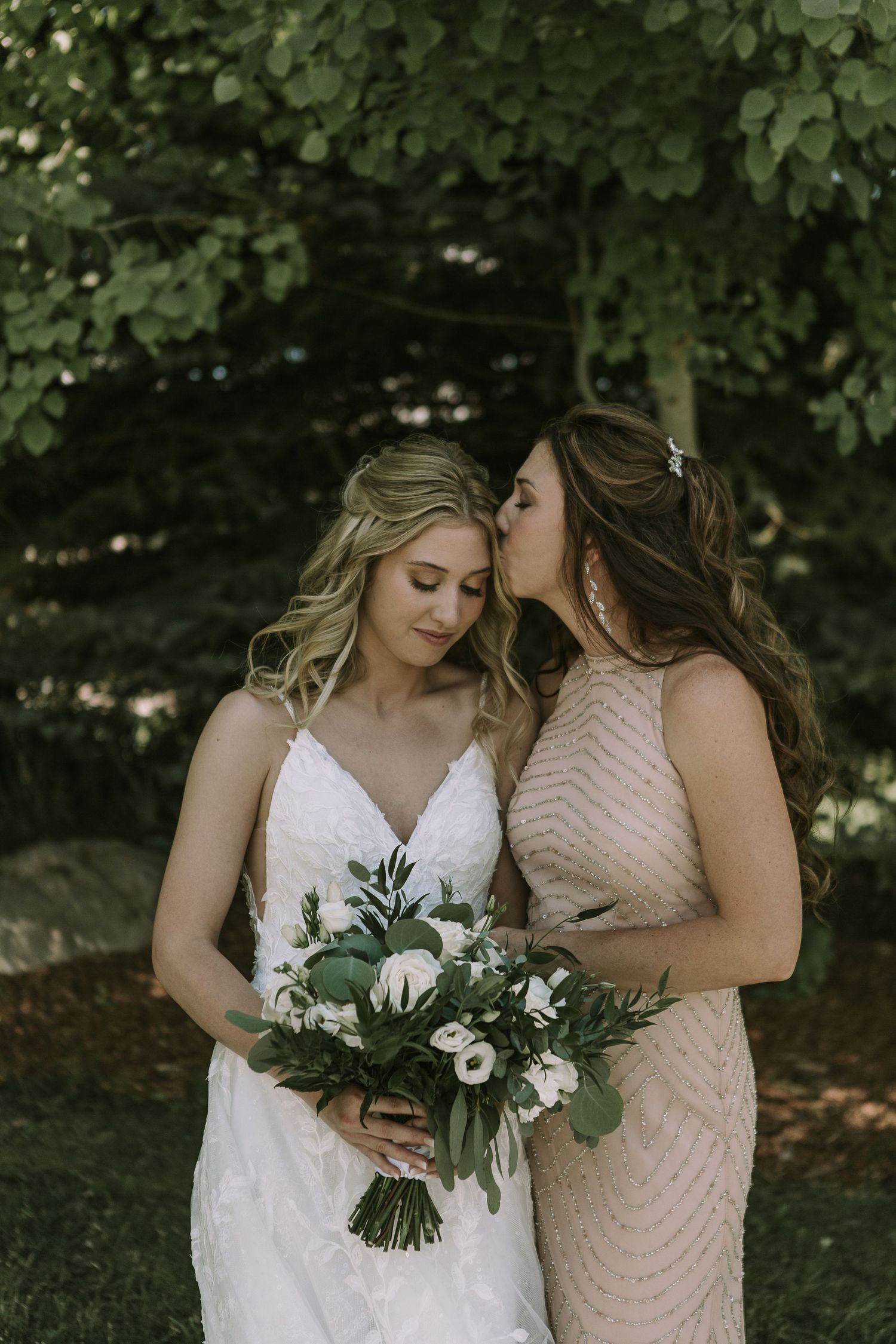 Two women in formal dresses share an intimate moment with white floral bouquet.