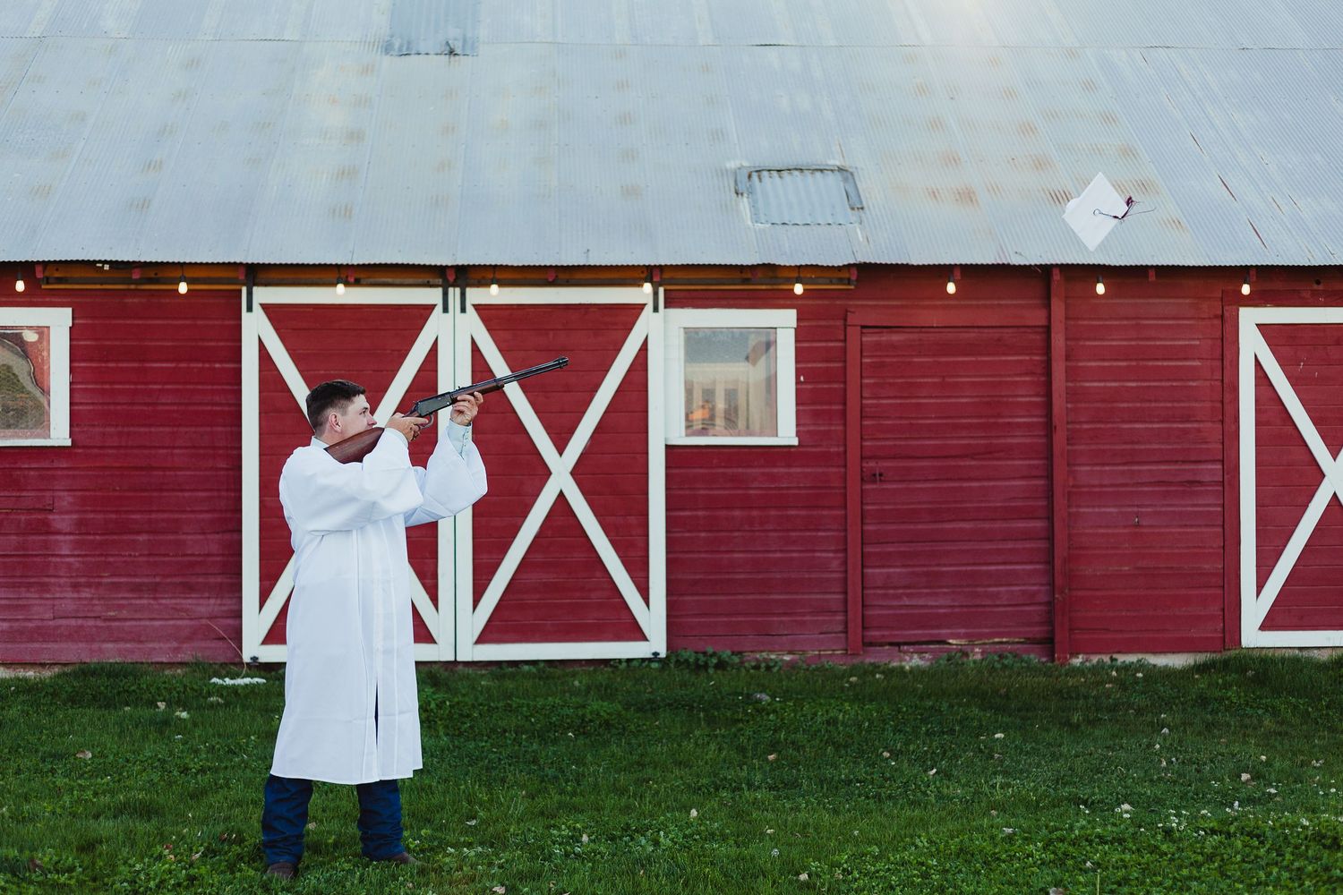 Person in white coat reaching up to light fixture on red barn exterior.