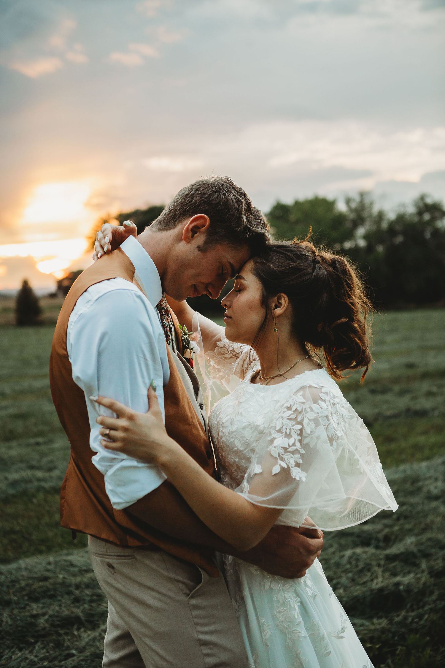 A tender sunset moment between newlyweds in a grassy field.