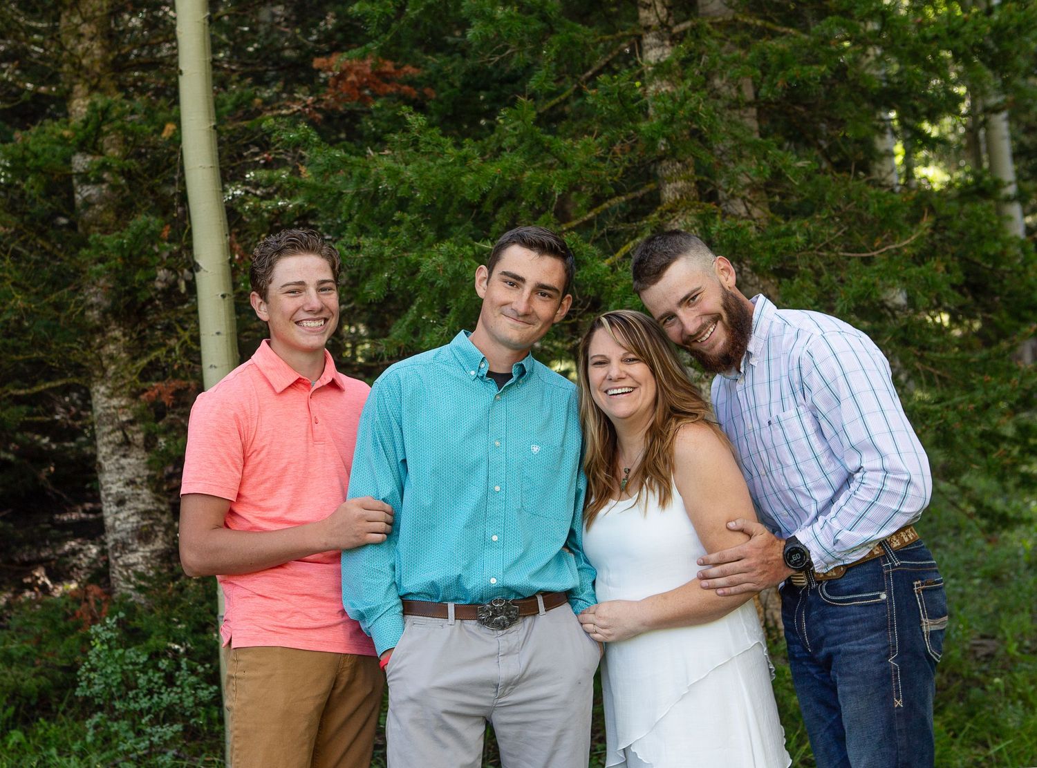 Group poses casually together against lush forest backdrop wearing bright summer colors.