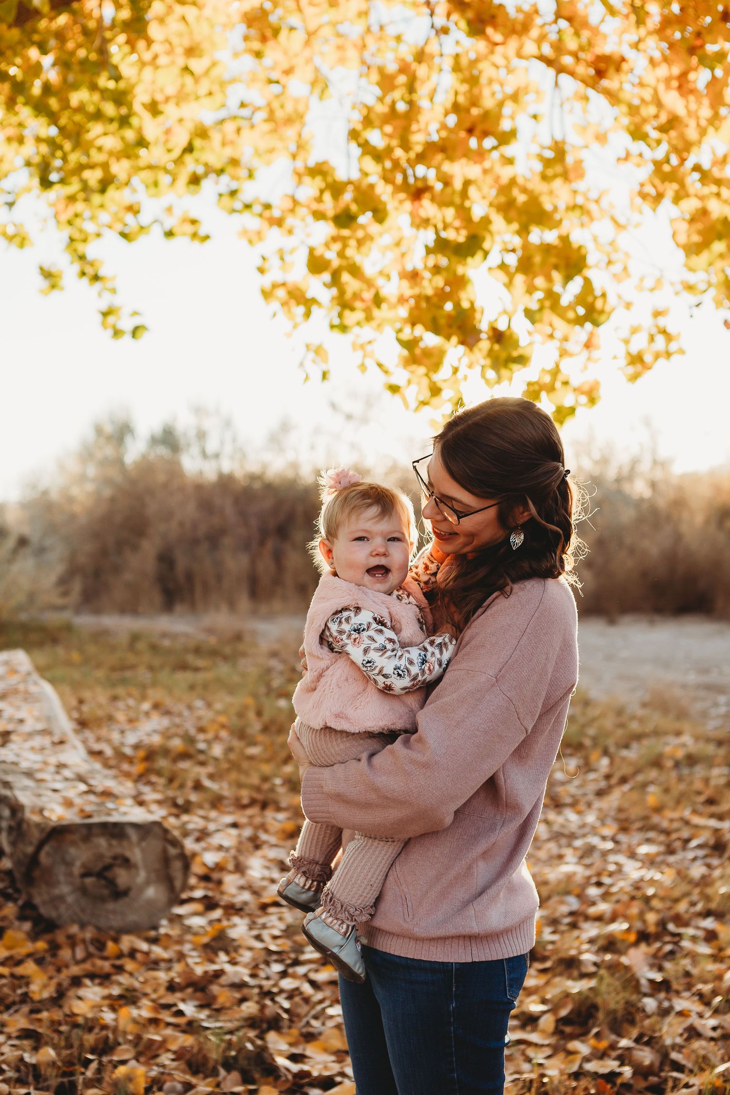 Joyful autumn moment shared between two people in pink and floral outfits under golden trees.