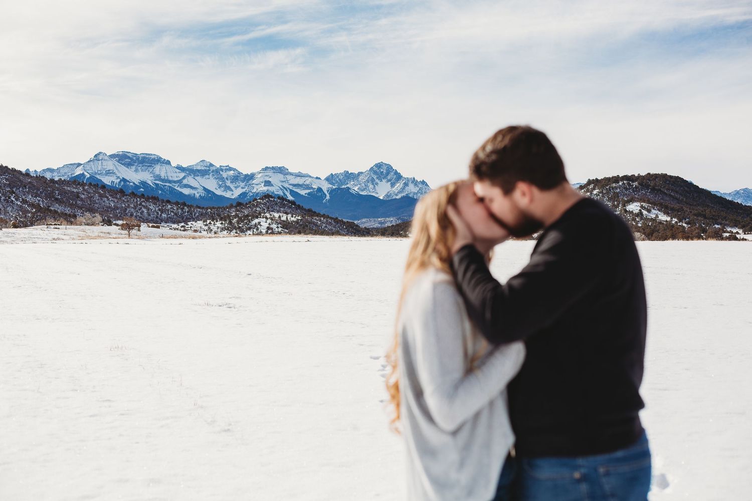 A couple sharing an intimate moment against a snowy mountain landscape backdrop.
