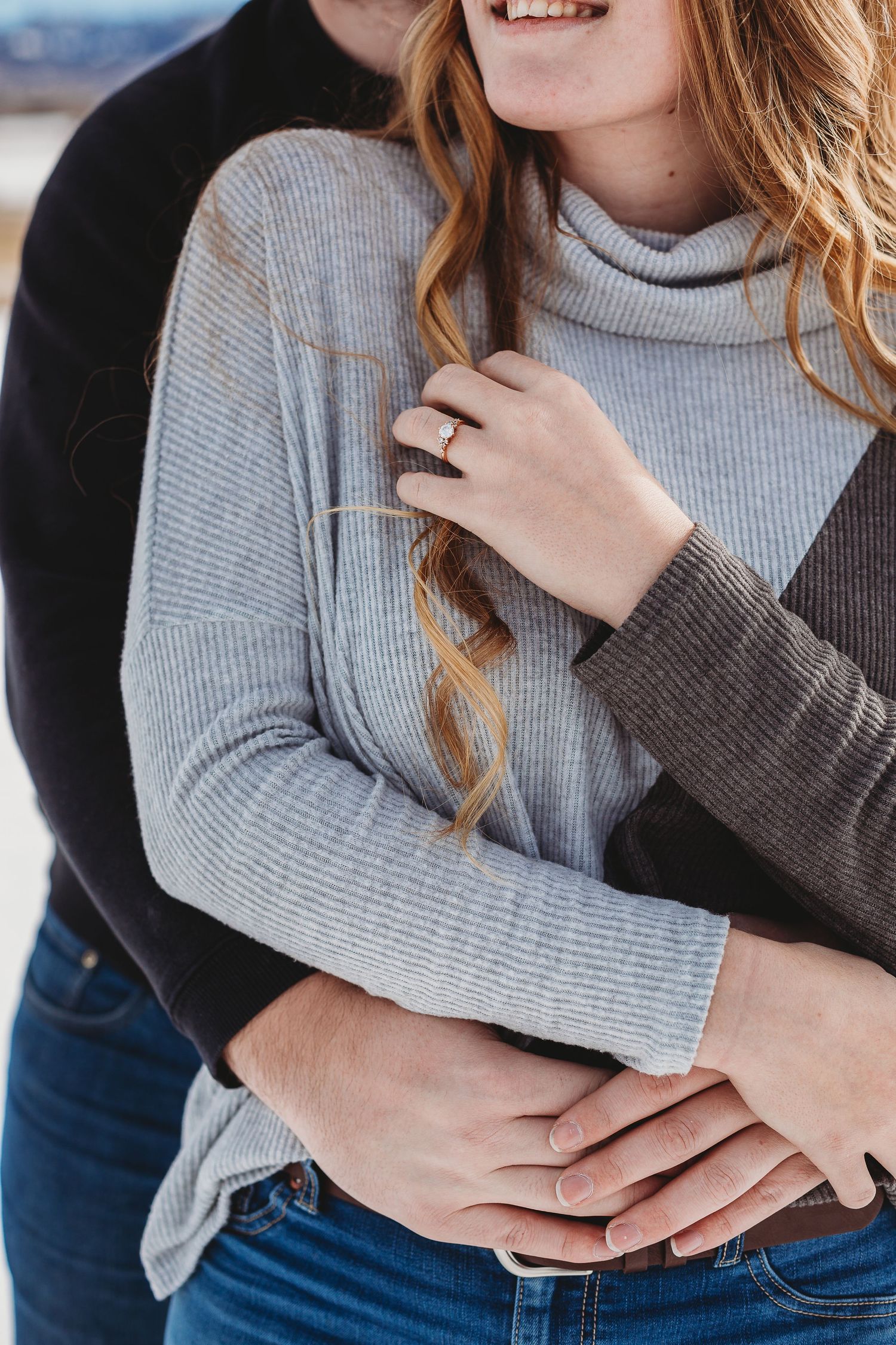 A cozy engagement photo showing a ring and grey sweater in natural light.