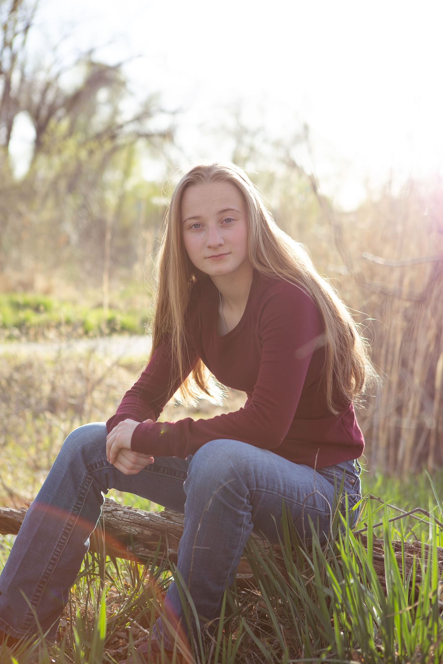 Person in burgundy sweater sitting on wooden fence during golden hour portrait session.