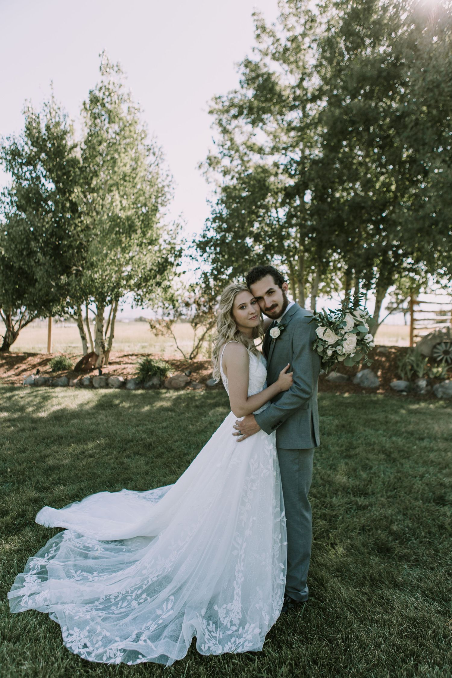 Elegant wedding portrait showcasing a beautiful lace gown and gray suit in a garden setting.