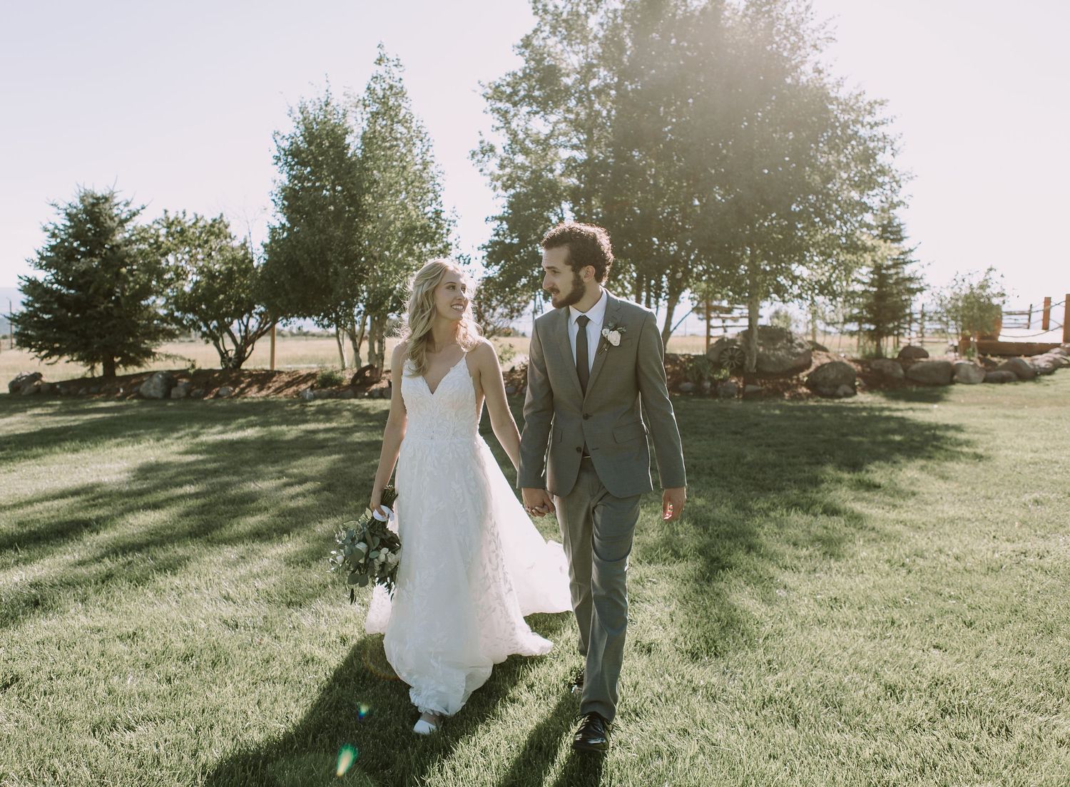 Newlyweds walking hand in hand through a sun-drenched garden on their wedding day.