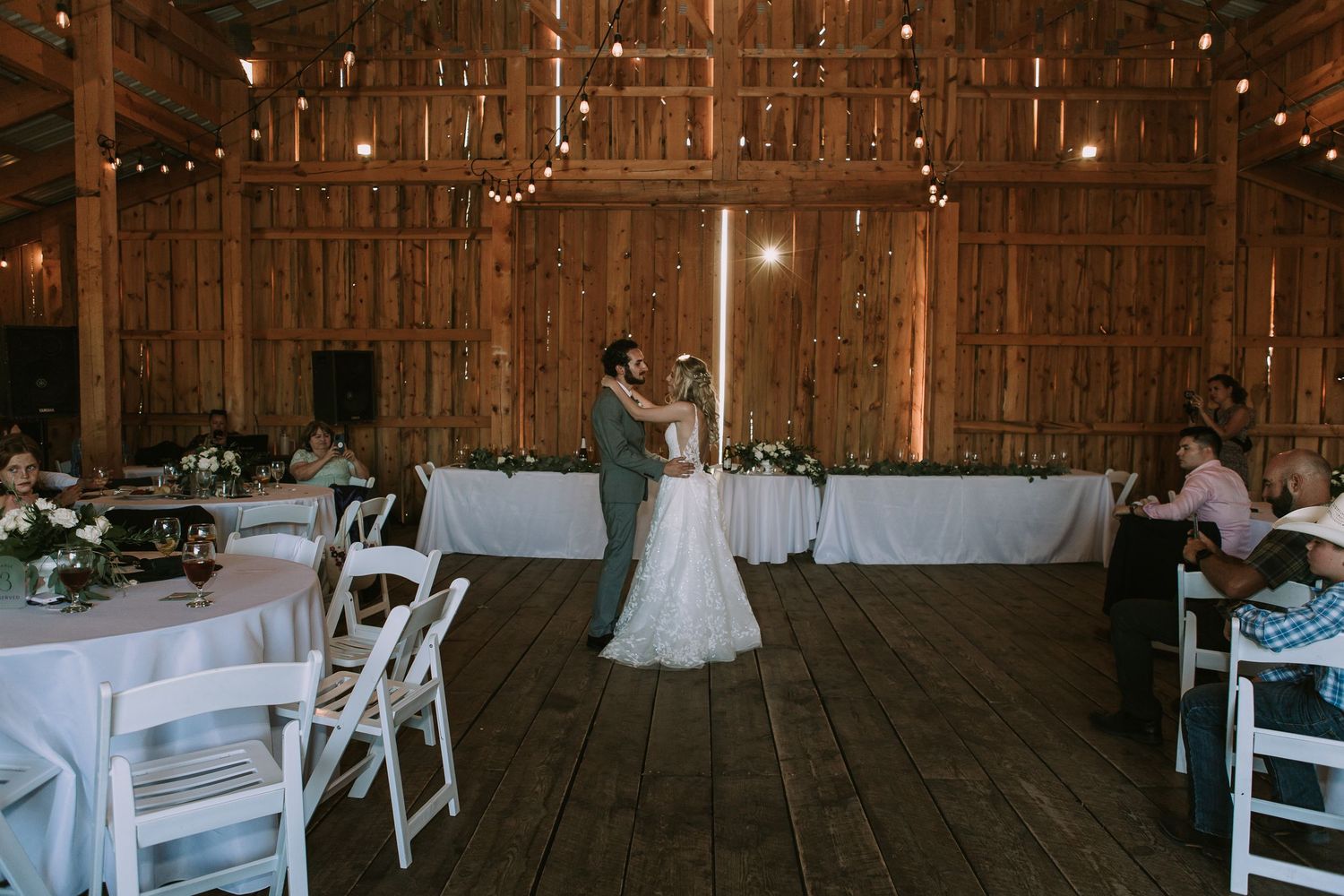 Couple dancing in rustic barn wedding venue surrounded by white chairs and tables.