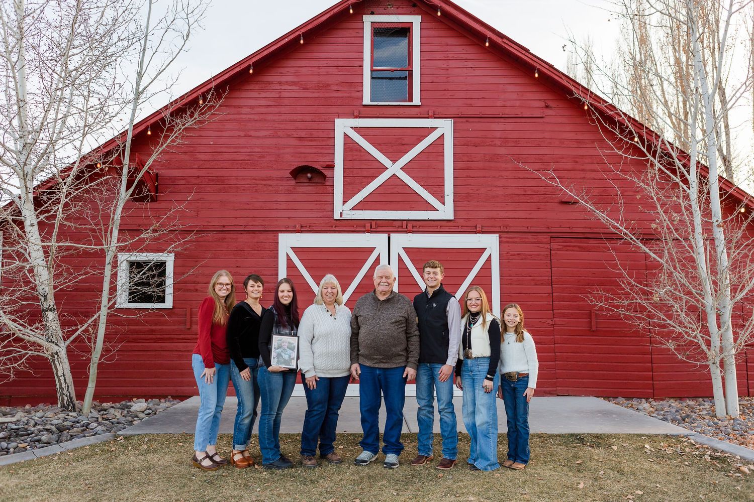 Group portrait in front of a classic red barn with white X-pattern doors during winter season.