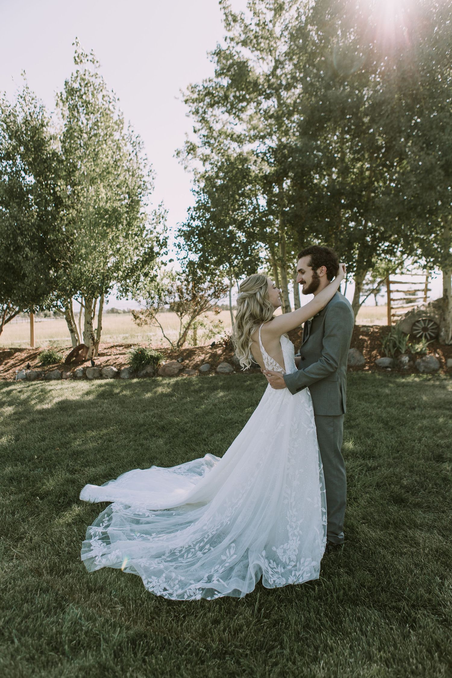 Sunlit garden wedding portrait showcasing detailed lace train against natural landscape.
