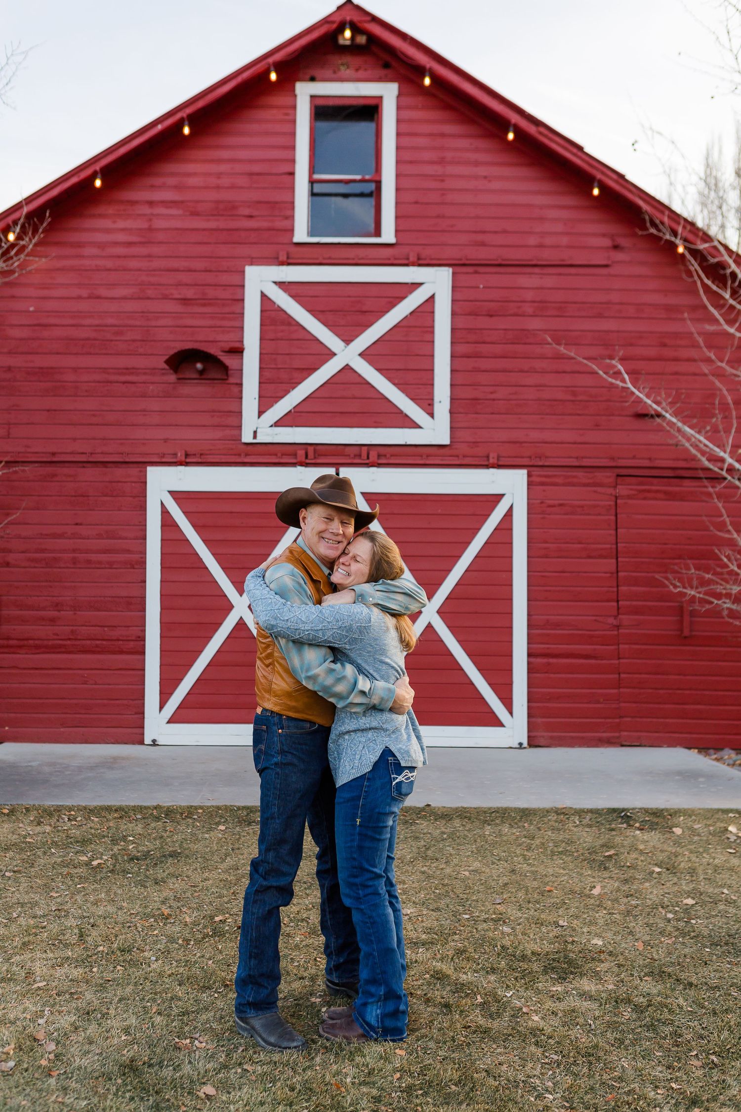 Romantic embrace in front of a traditional red barn with white geometric door patterns.