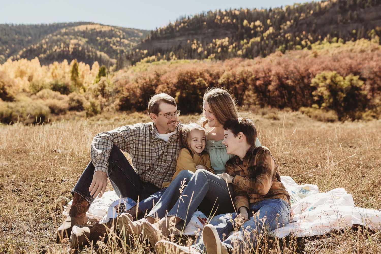 Cozy autumn engagement photo of couple relaxing in golden mountain meadow.