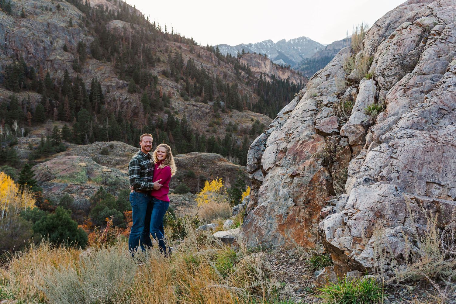 Outdoor portrait with mountain backdrop and fall foliage near large rocky outcrop.