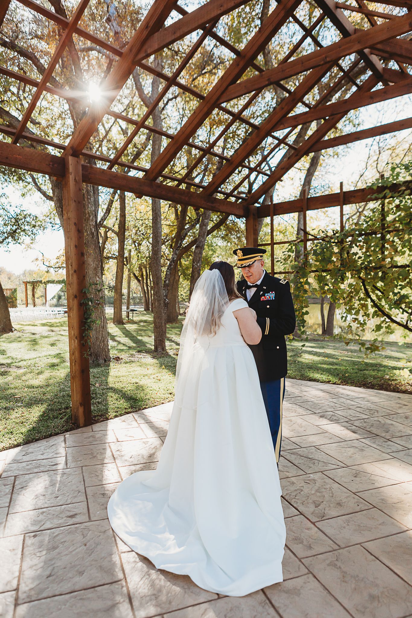 Couple shares intimate moment under wooden pergola during outdoor wedding ceremony.