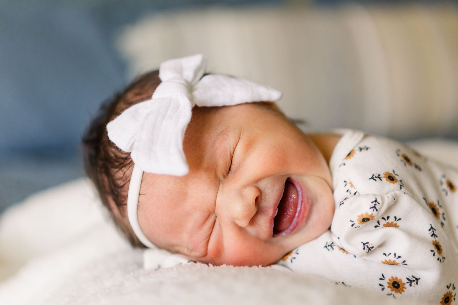 Sweet newborn baby in floral outfit and white bow headband sleeping peacefully.