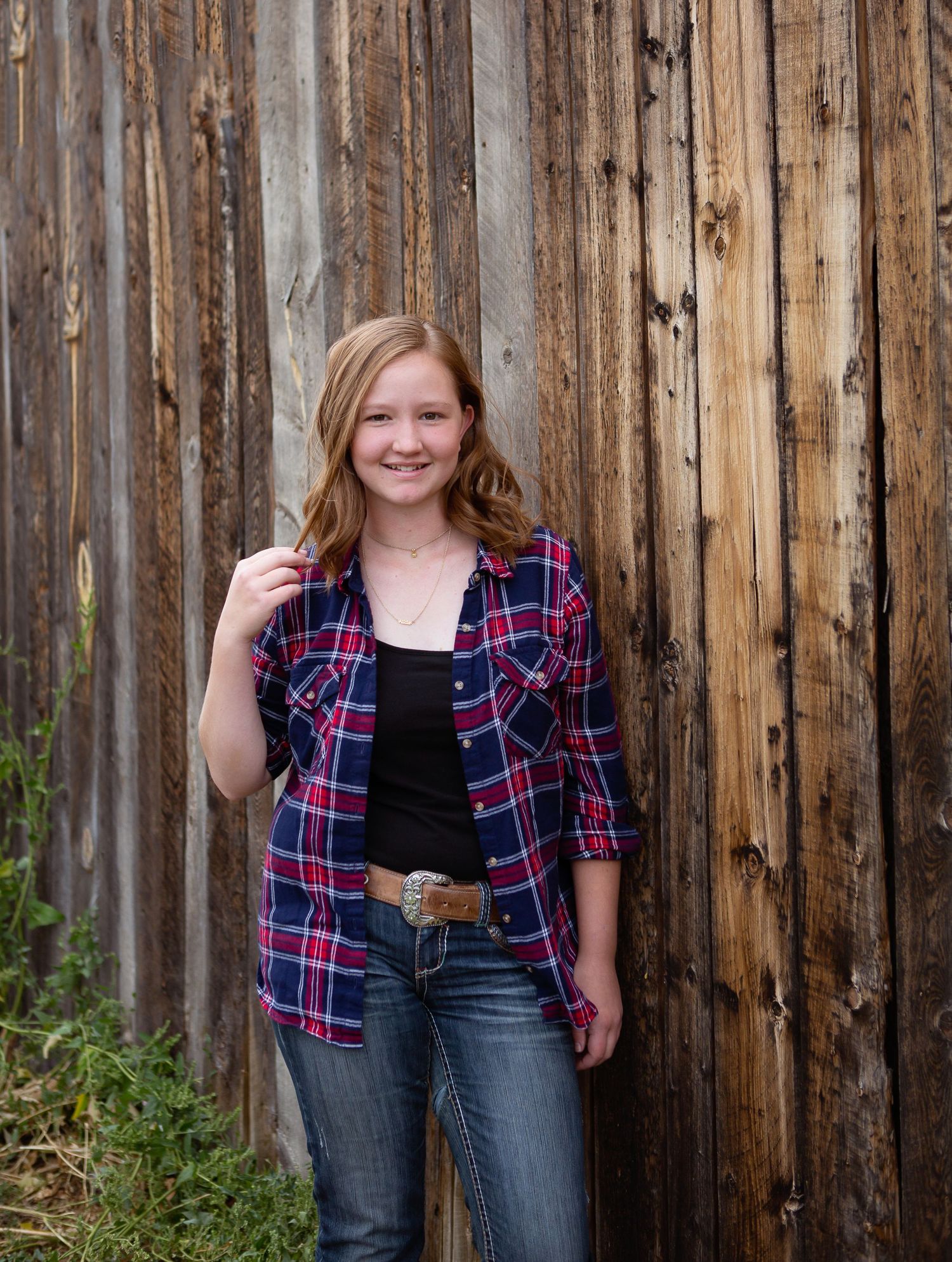 Person wearing plaid flannel shirt poses casually against weathered wooden fence.