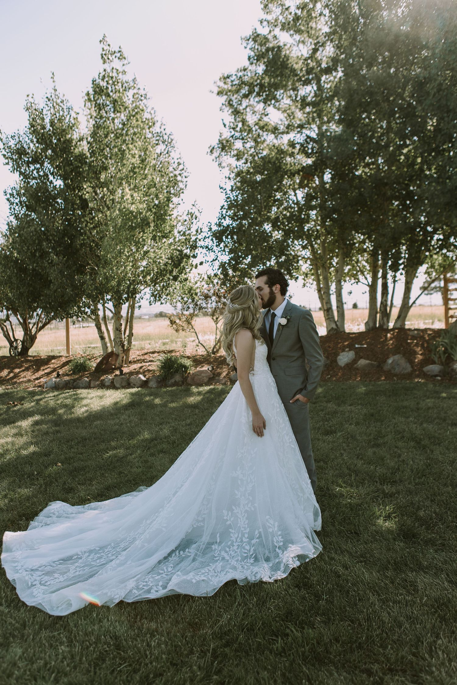 A romantic wedding portrait showing flowing lace train of bridal gown against natural outdoor backdrop.