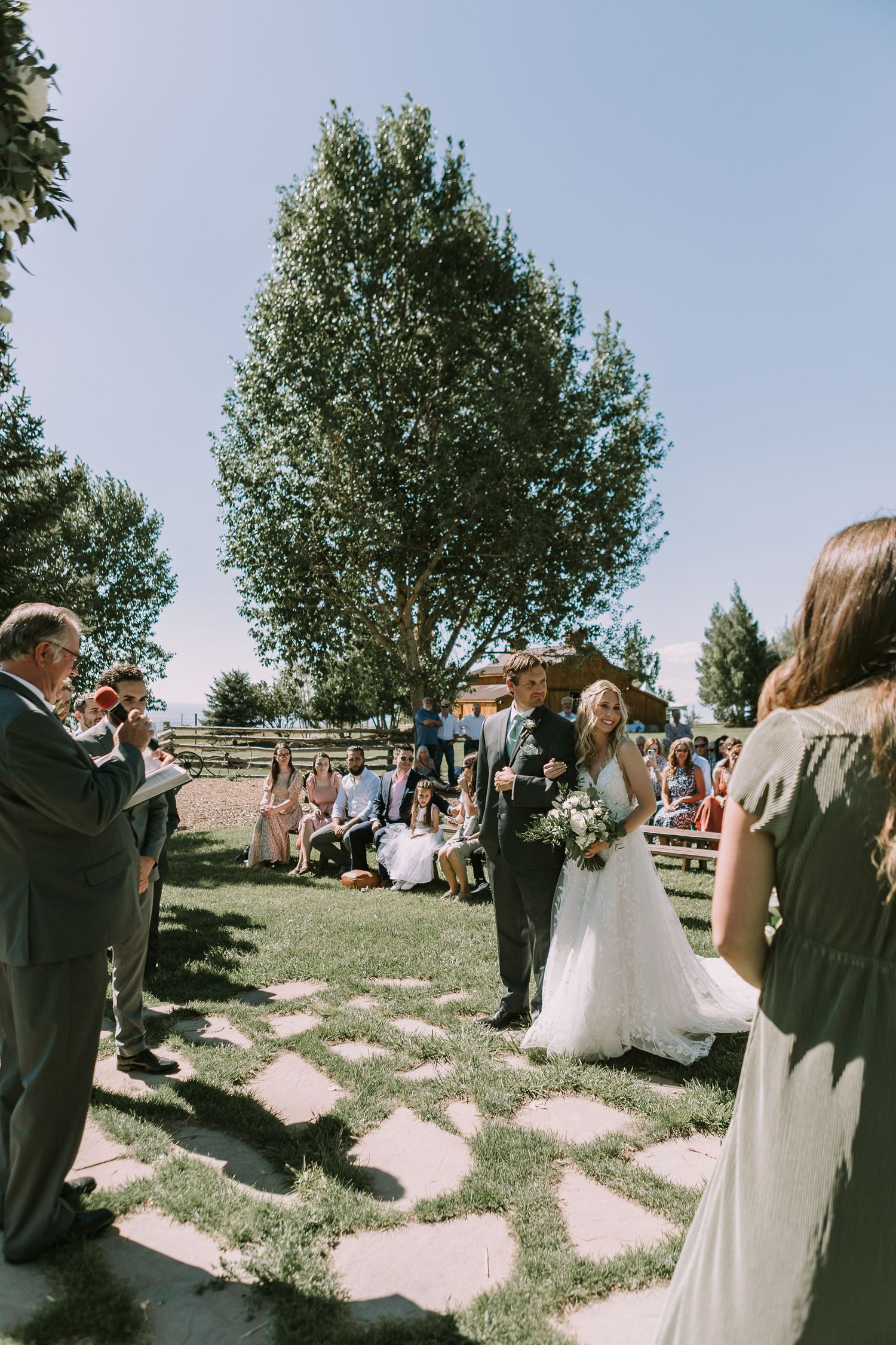 Summer wedding ceremony on stone pathway with mountain landscape backdrop.