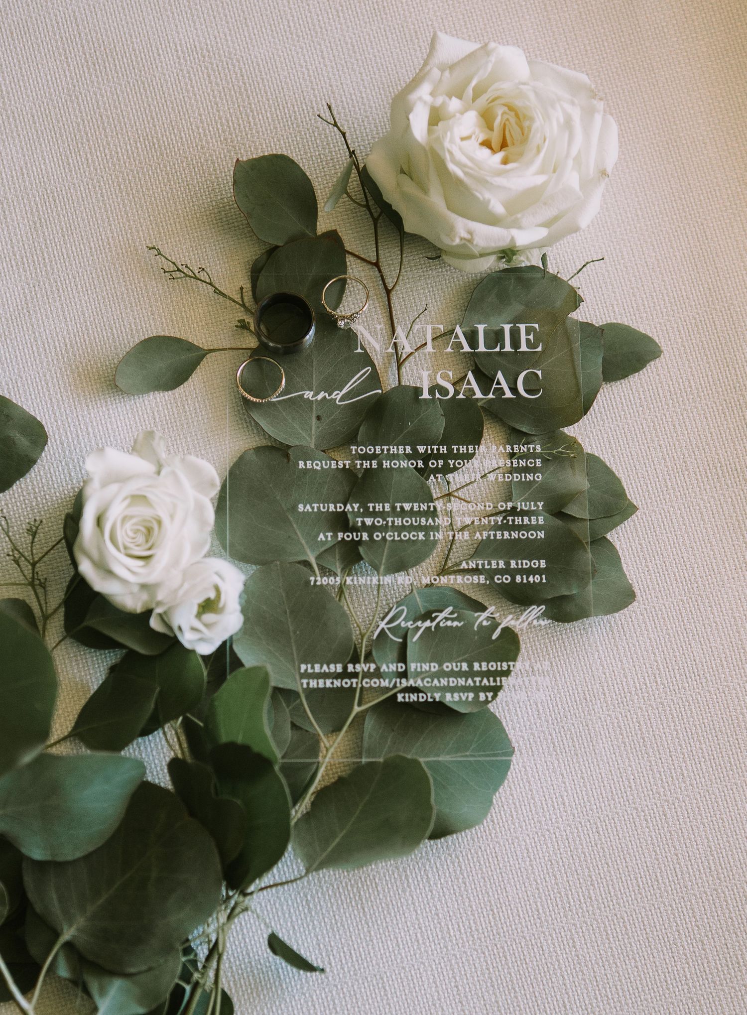 Elegant acrylic wedding invitation with white roses and eucalyptus leaves.