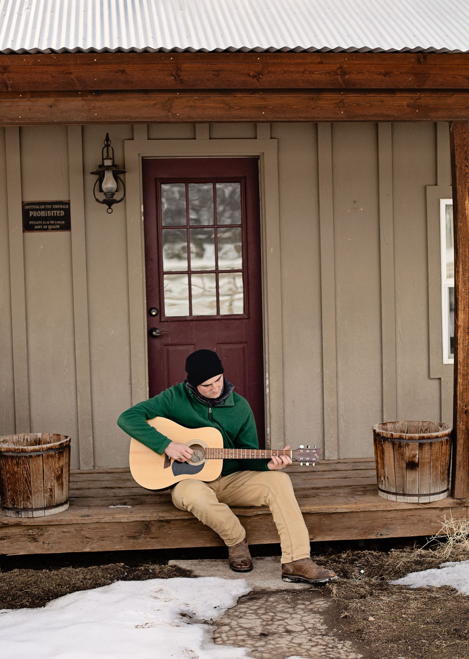 Person playing acoustic guitar while sitting on rustic wooden porch in winter.