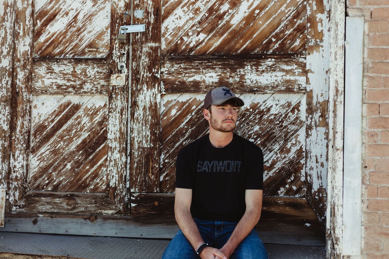 Person in black t-shirt sitting in front of weathered wooden door.