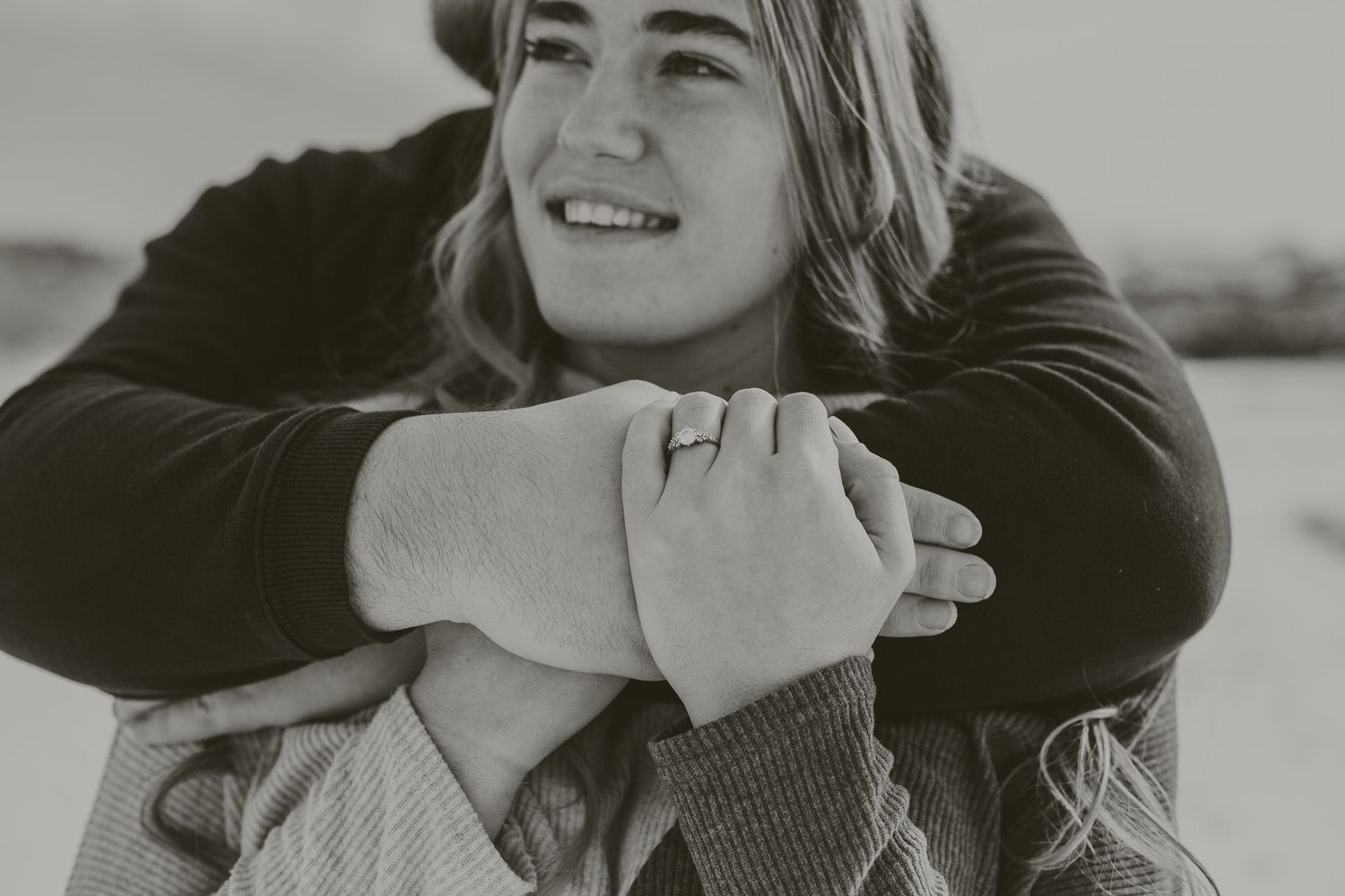 Close up portrait of a person joyfully smiling while being embraced from behind.