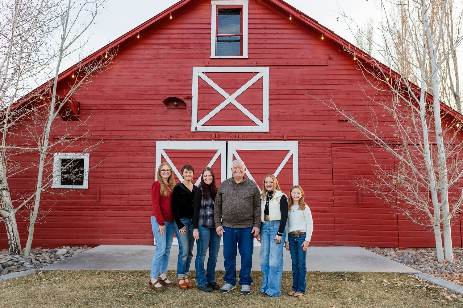 A casual group portrait in front of a red barn featuring white X-shaped architectural details.