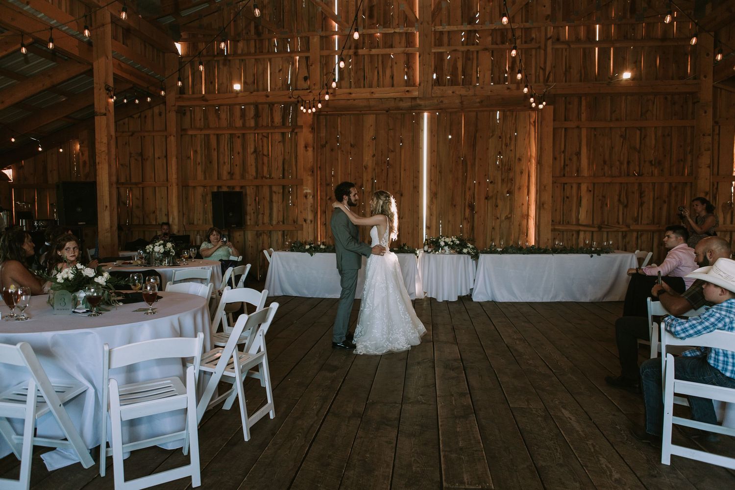 Wedding reception in rustic barn venue with white chairs and tables arranged for celebration.