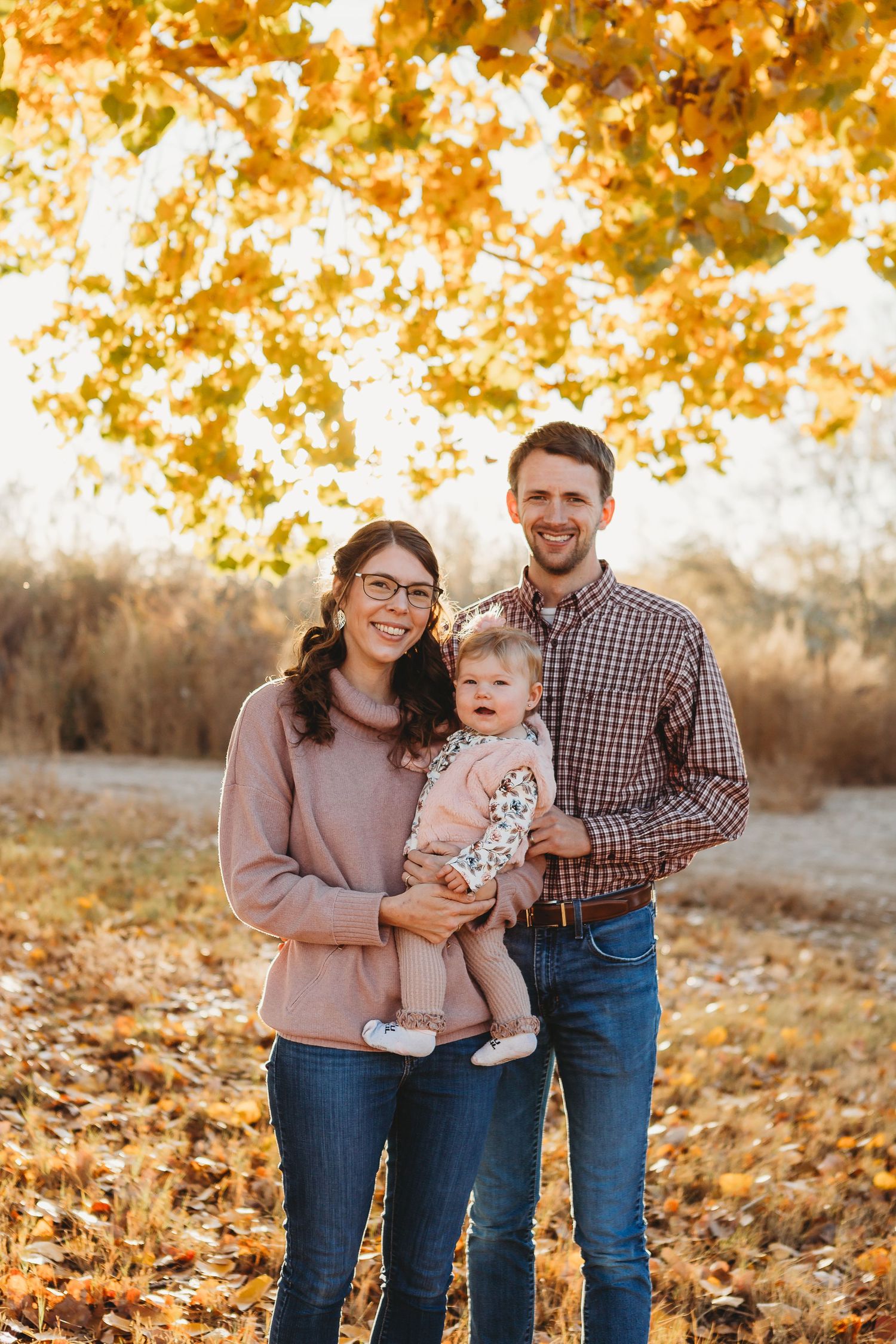 A heartwarming autumn family portrait with golden leaves in the background during sunset.