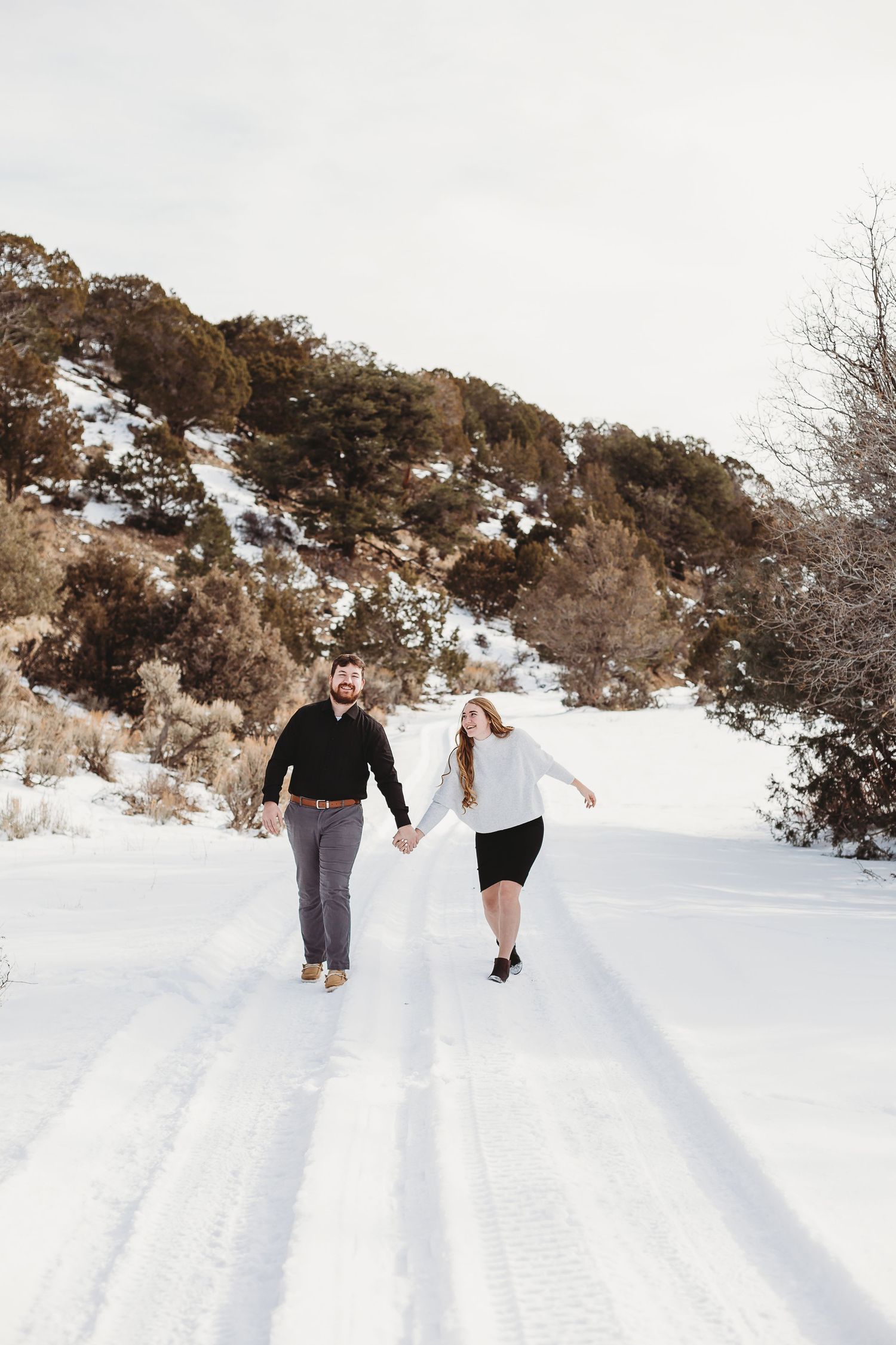 Couple holding hands while walking on a snow-covered mountain path.