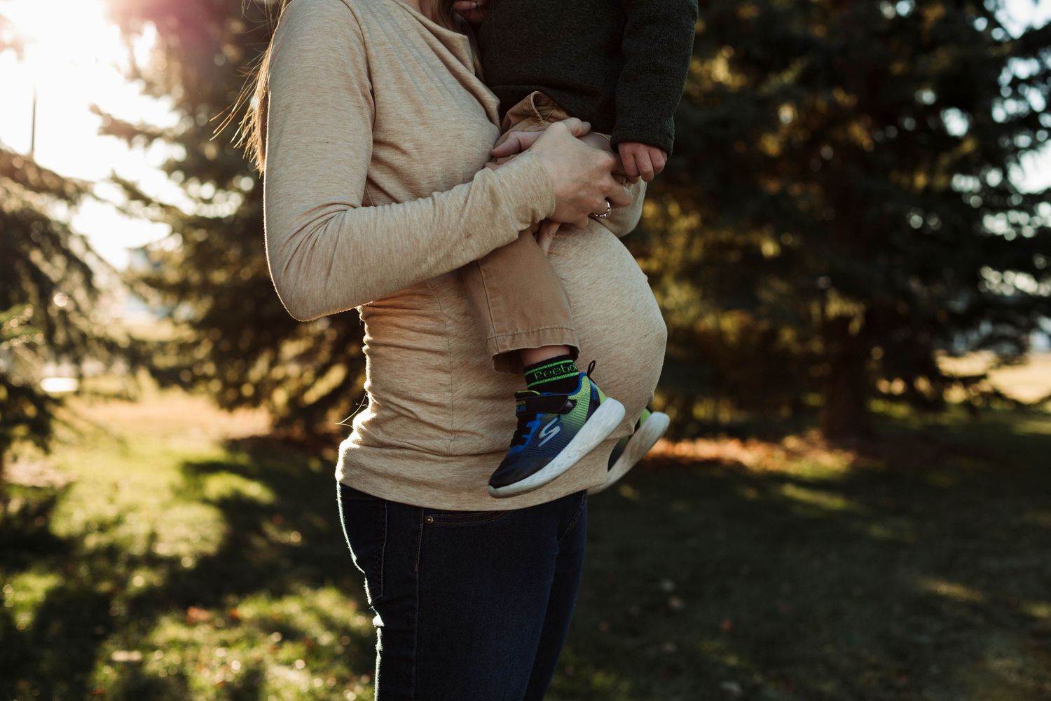 Side view of pregnant woman's belly highlighted by natural sunlight in outdoor setting.