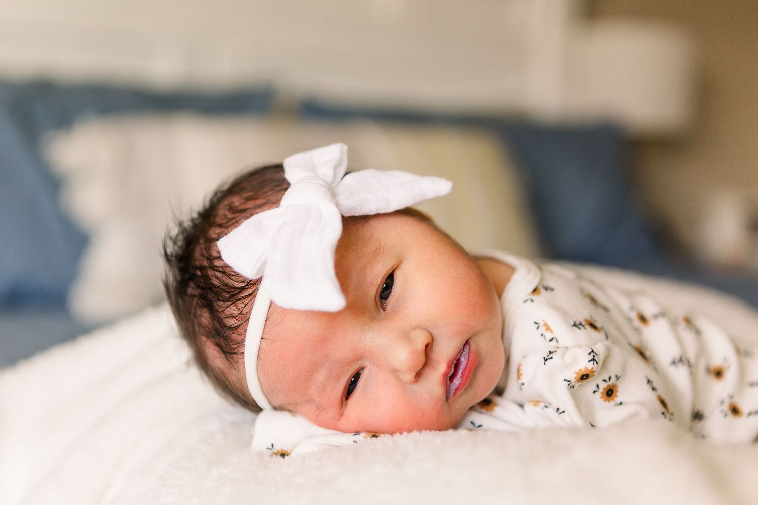 Sleeping baby wearing white bow headband on light bedding.