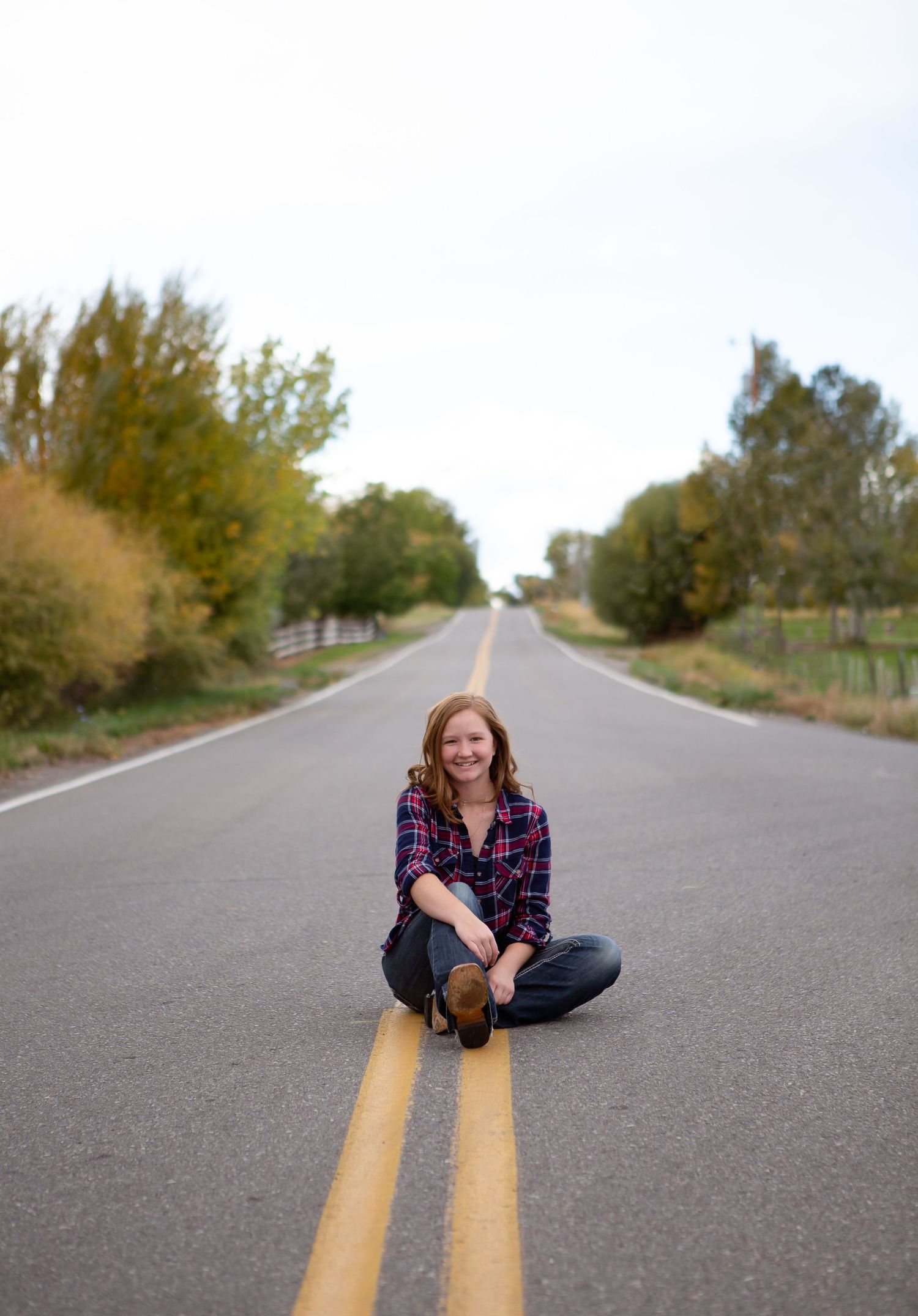 Person in plaid shirt sits on yellow road lines of empty rural highway.
