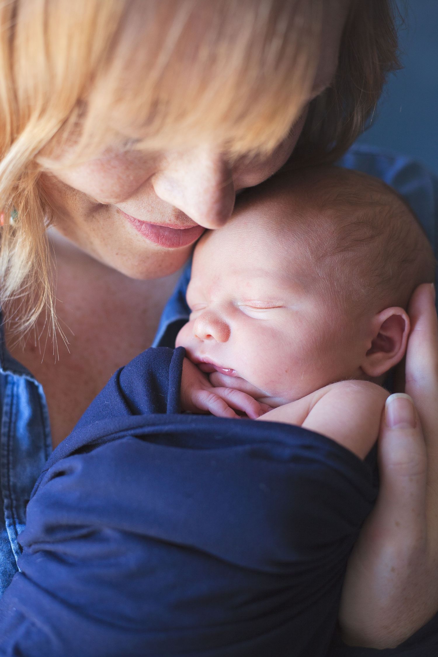 An intimate closeup of a tender moment between parent and sleeping baby in blue.