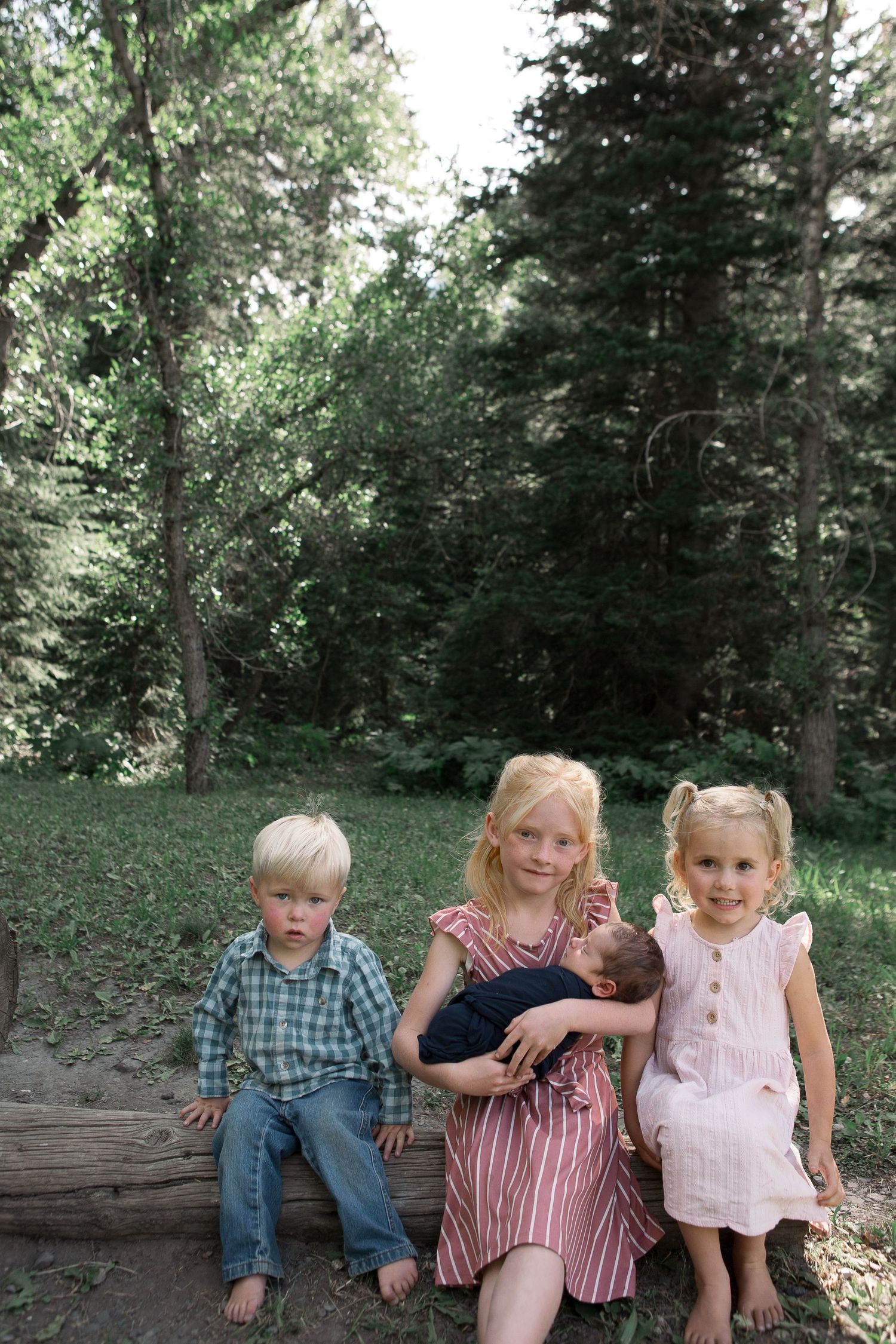 Children sit together on a fallen log in a wooded area during summer.