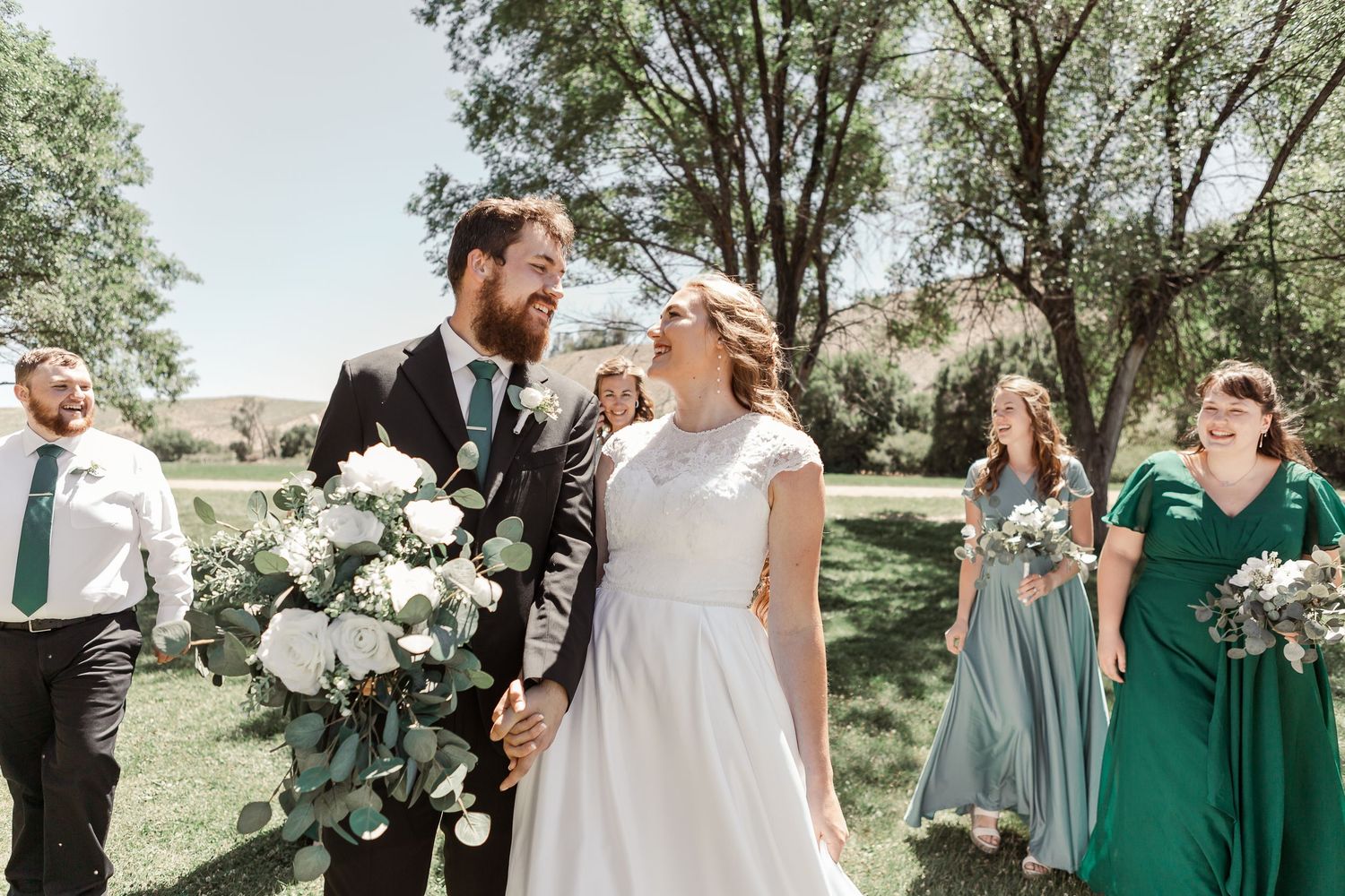 Wedding party laughing together during outdoor photo session under sunny skies.