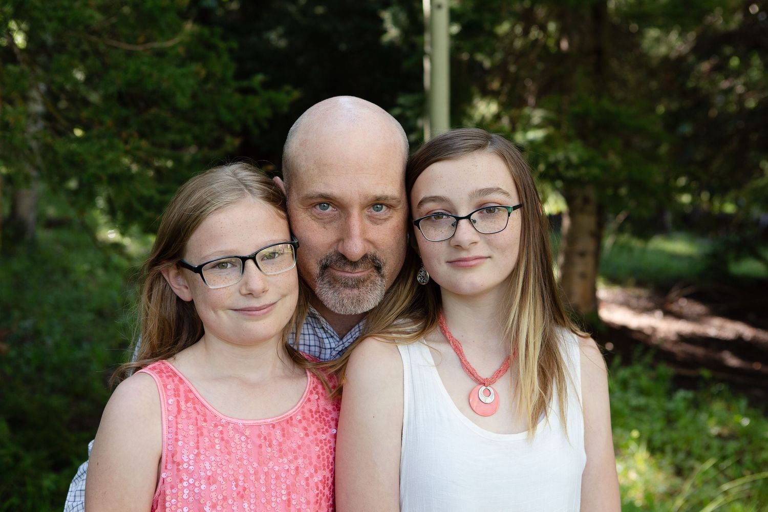 Three people in casual attire pose for a portrait with trees in the background.