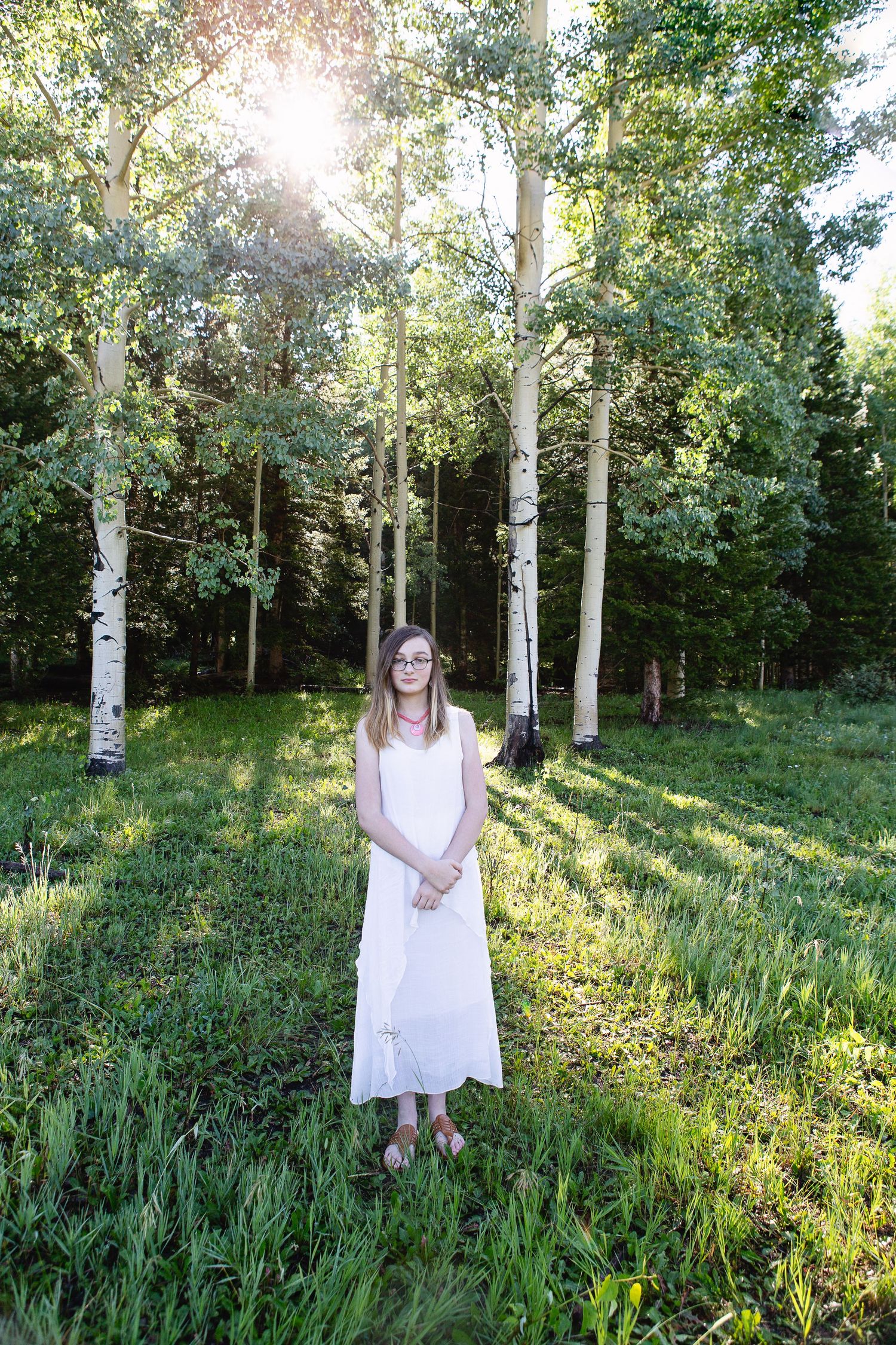 Person in white dress stands in serene aspen grove with dappled sunlight.