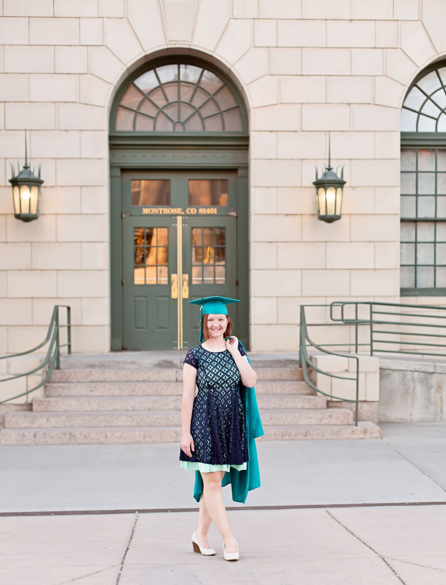 Graduate in polka dot dress and teal gown poses in front of historic building entrance.