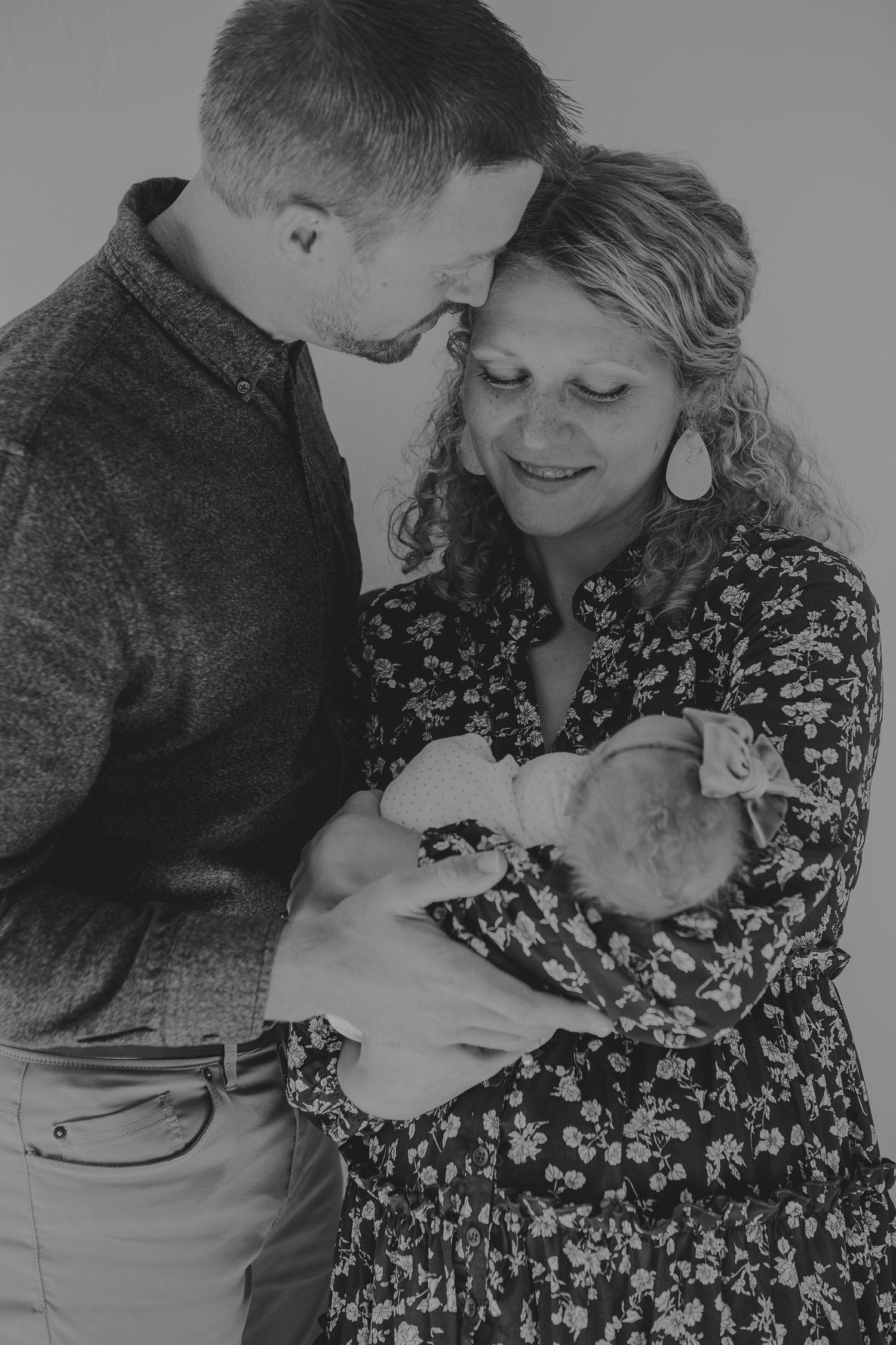 Black and white photo of parents sharing an intimate moment with their newborn baby.