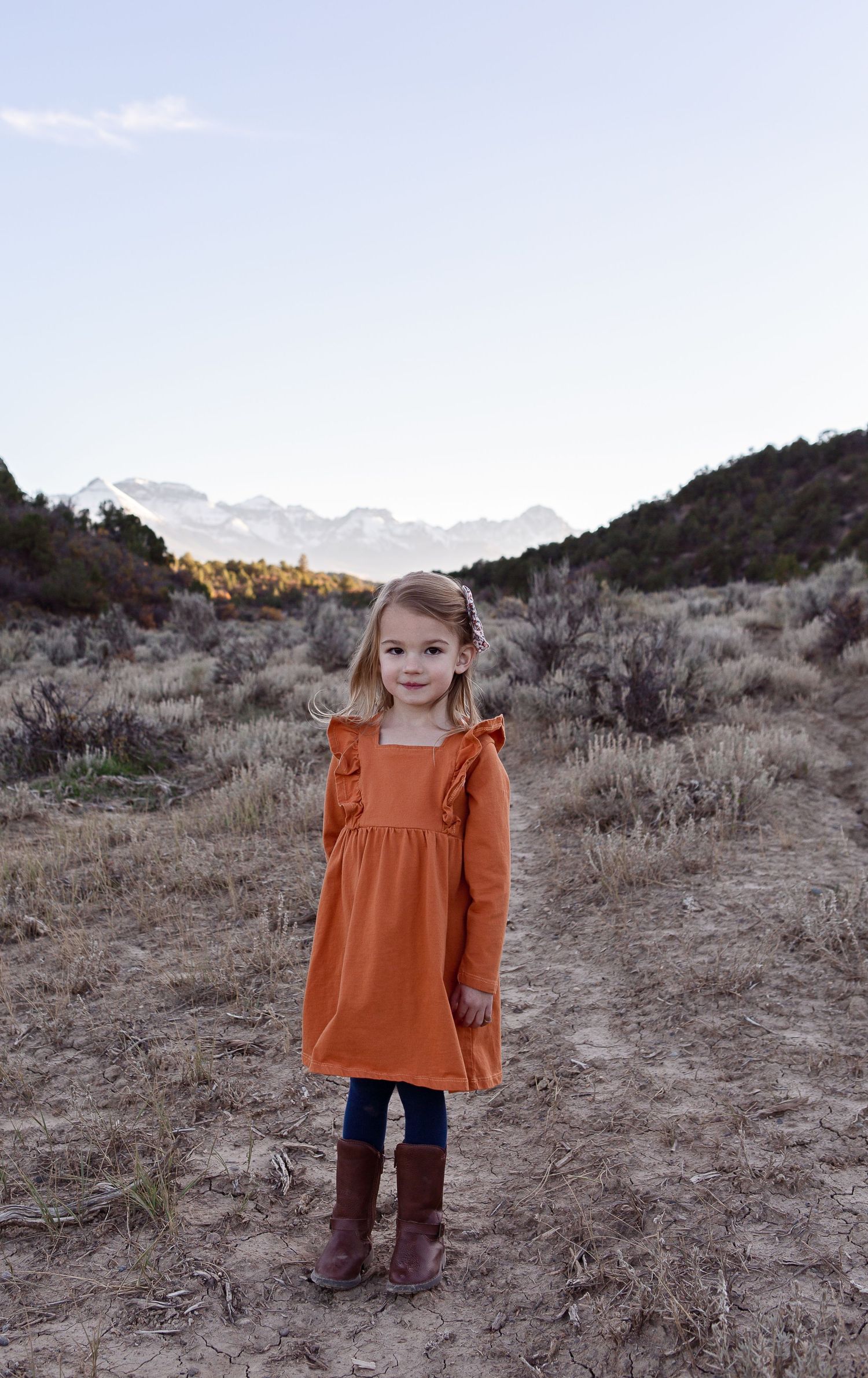 A rustic outdoor portrait showing a burnt orange dress against a mountainous desert landscape.