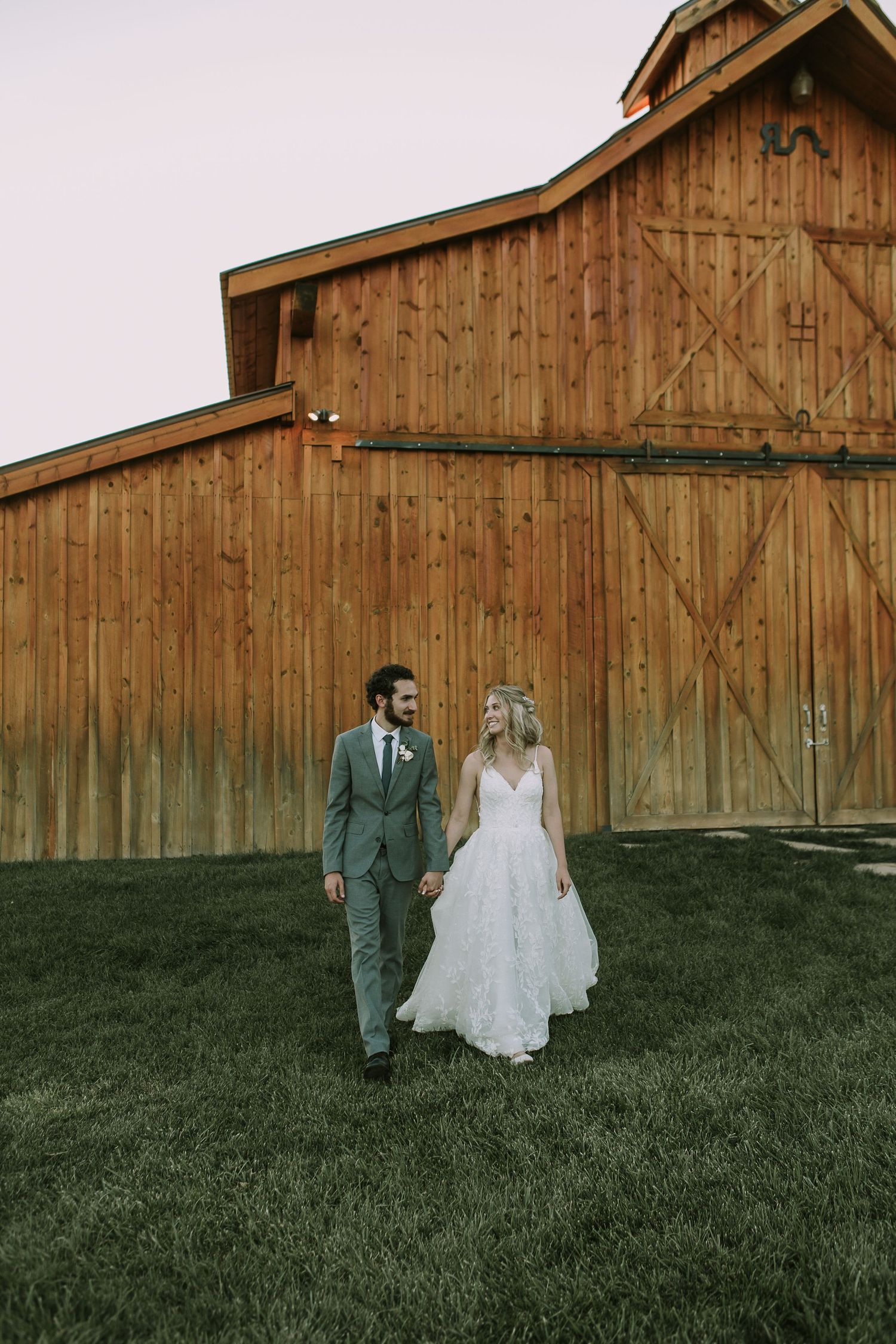 Wedding couple poses in front of rustic wooden barn wearing elegant attire.