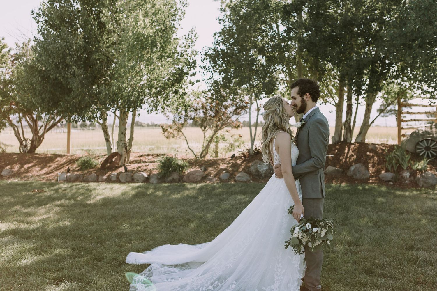 Wedding portrait in natural light with flowing lace train against garden landscape.